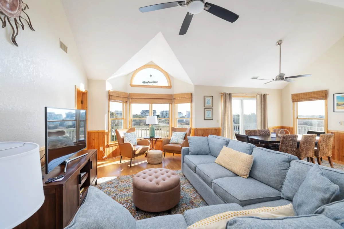 A bright living room with seating arranged around a coffee table and large windows.