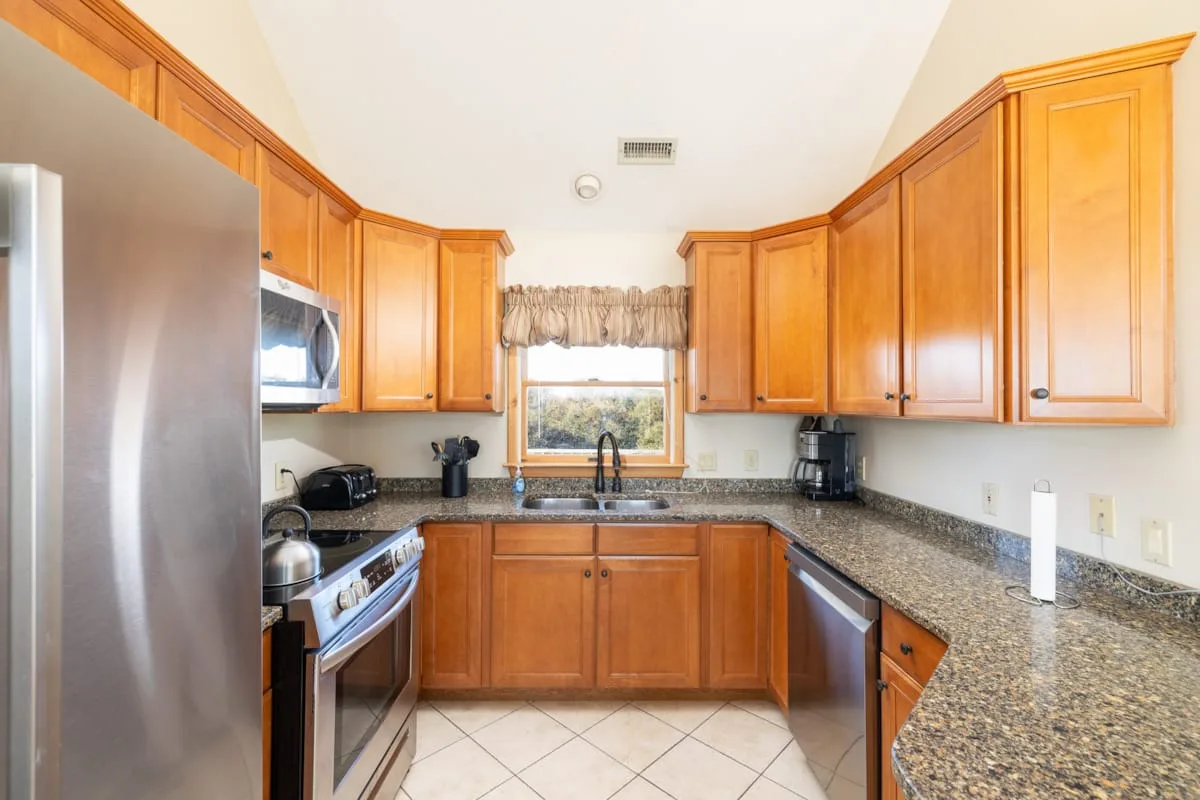 A kitchen with wooden cabinets, granite counters, and a window above the sink.