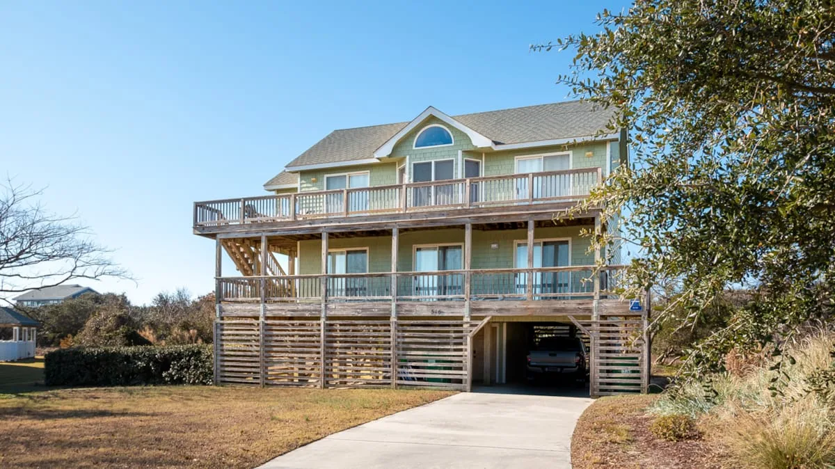 A two-story house with a broad wooden deck and a driveway leading to the garage.