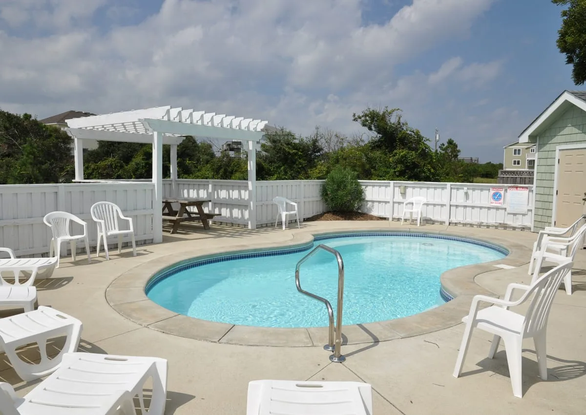 An outdoor swimming pool is surrounded by white seating and a fenced patio.