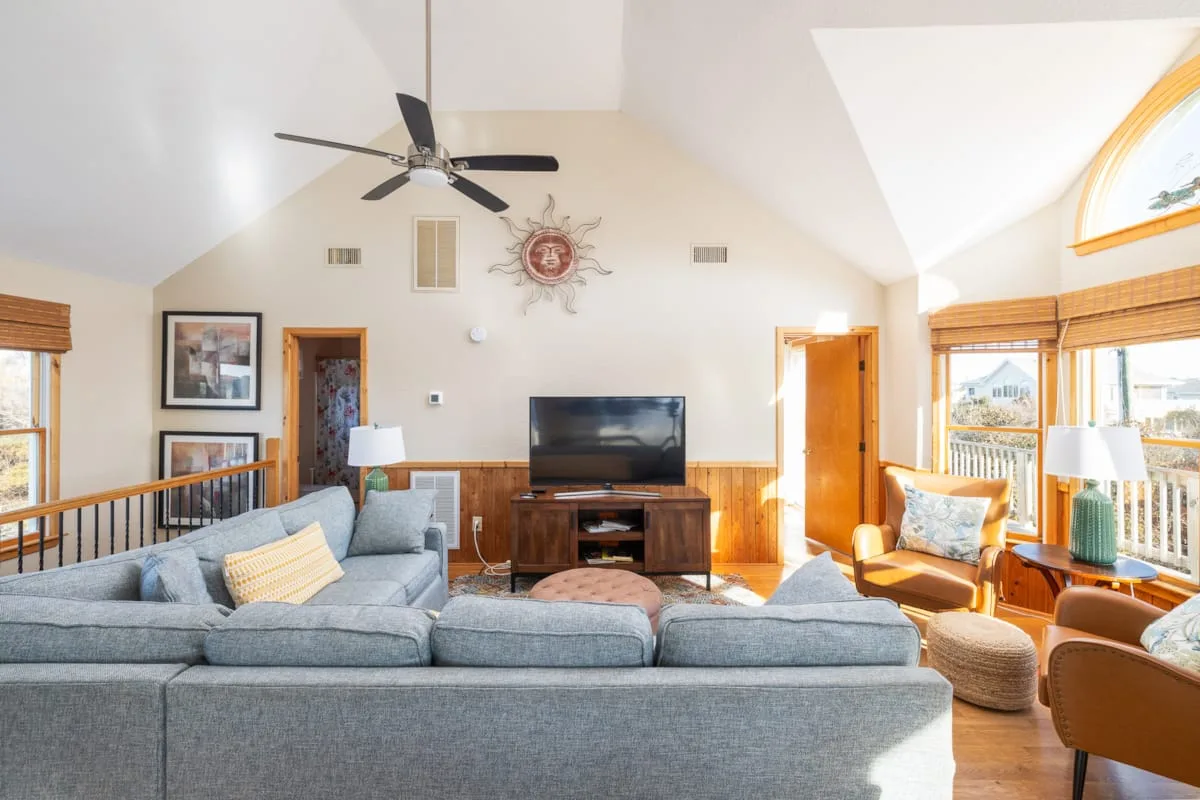 A bright living room with seating arranged around a television and large windows.