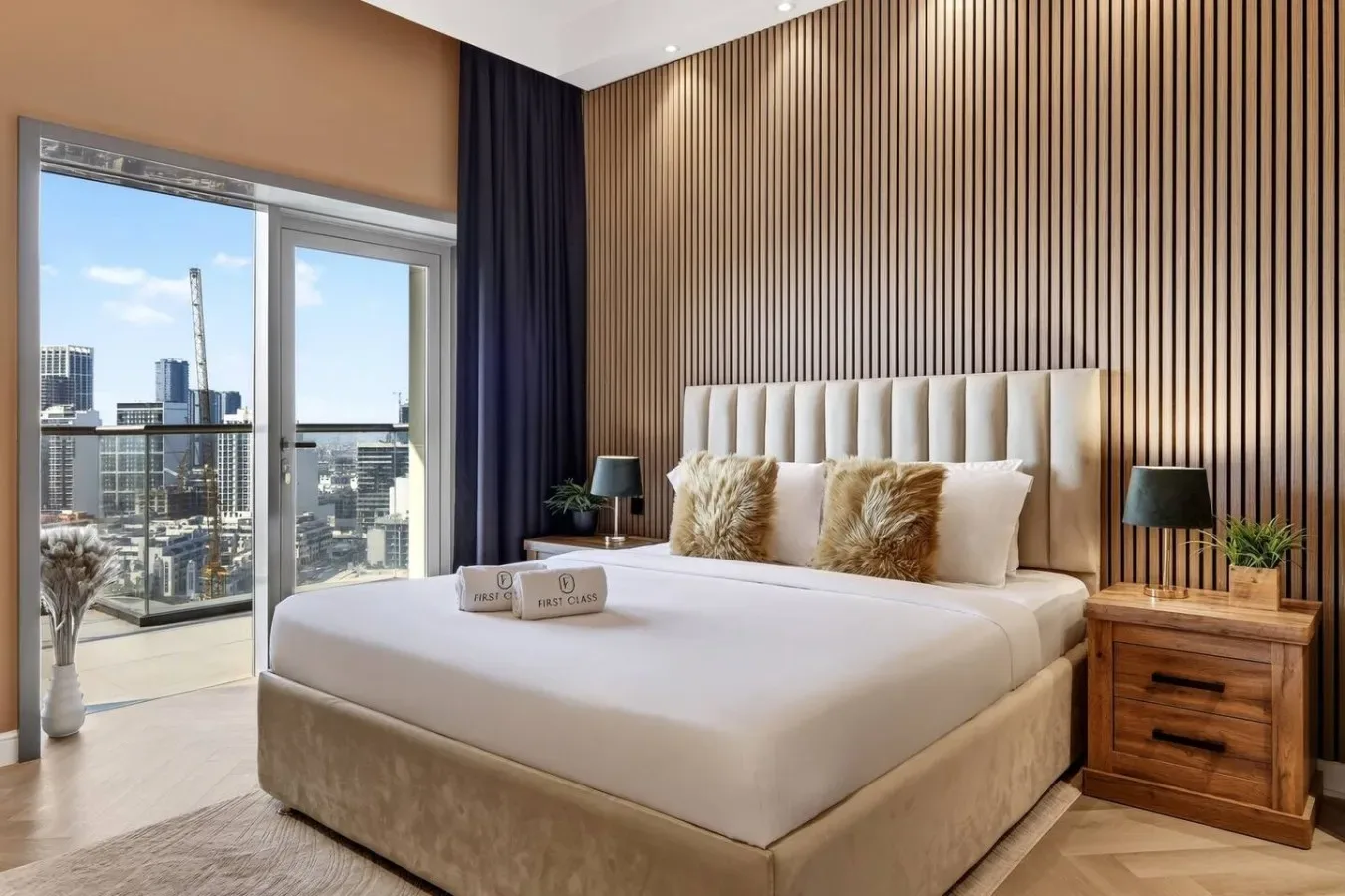 Un dormitorio con una cama grande, mesitas de noche y vistas de la ciudad a través de puertas de vidrio.