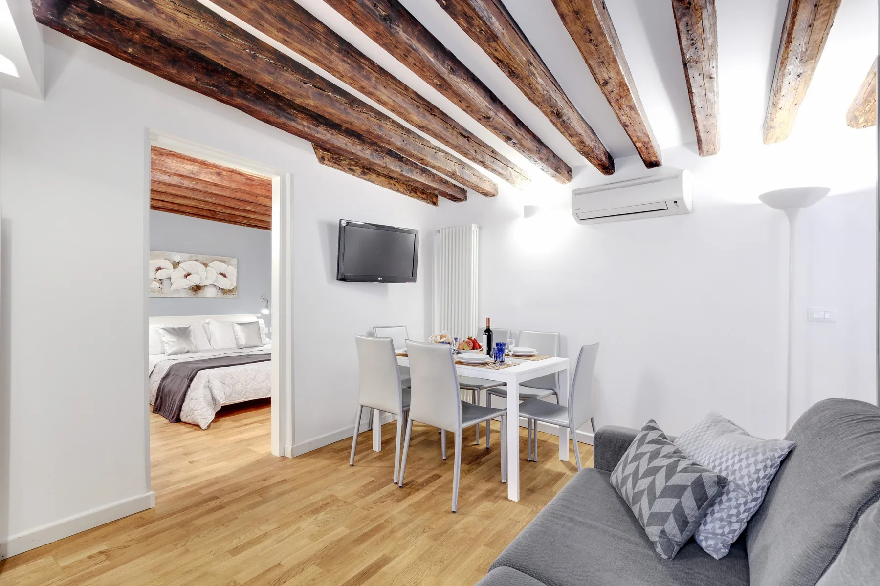 A bright living and dining area with exposed wooden ceiling beams and a gray sofa.