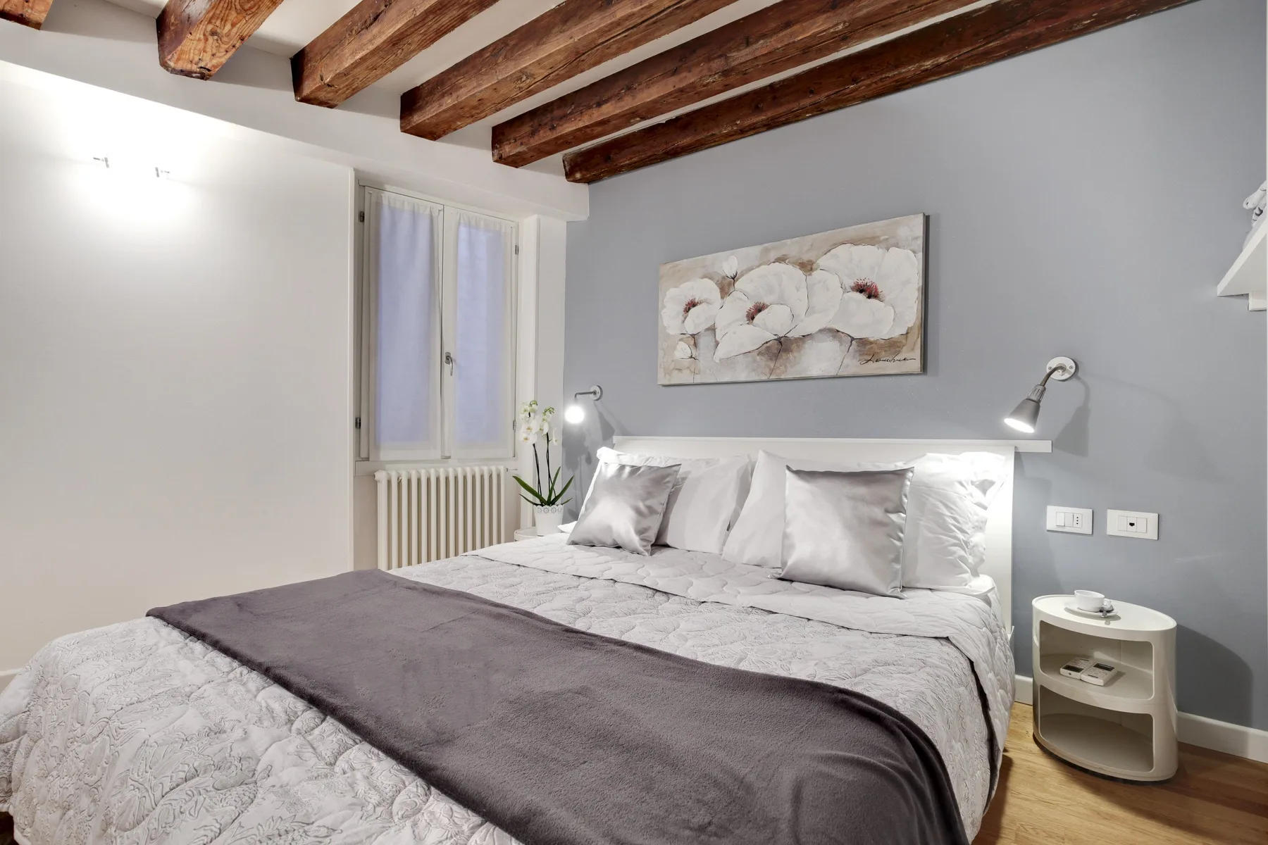 A bedroom with a neatly made bed beneath exposed wooden ceiling beams.
