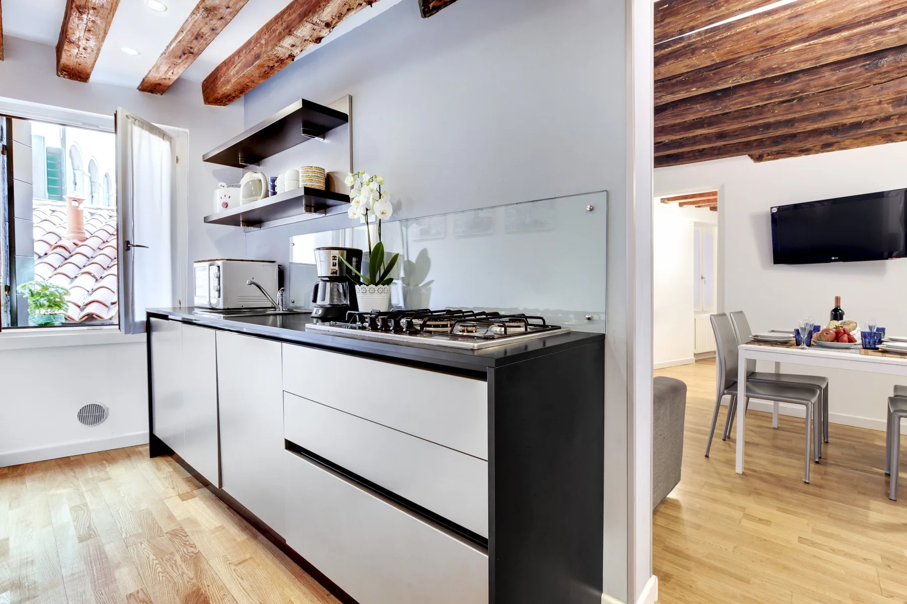 A modern kitchen with dark cabinets and a dining table in the adjoining room.