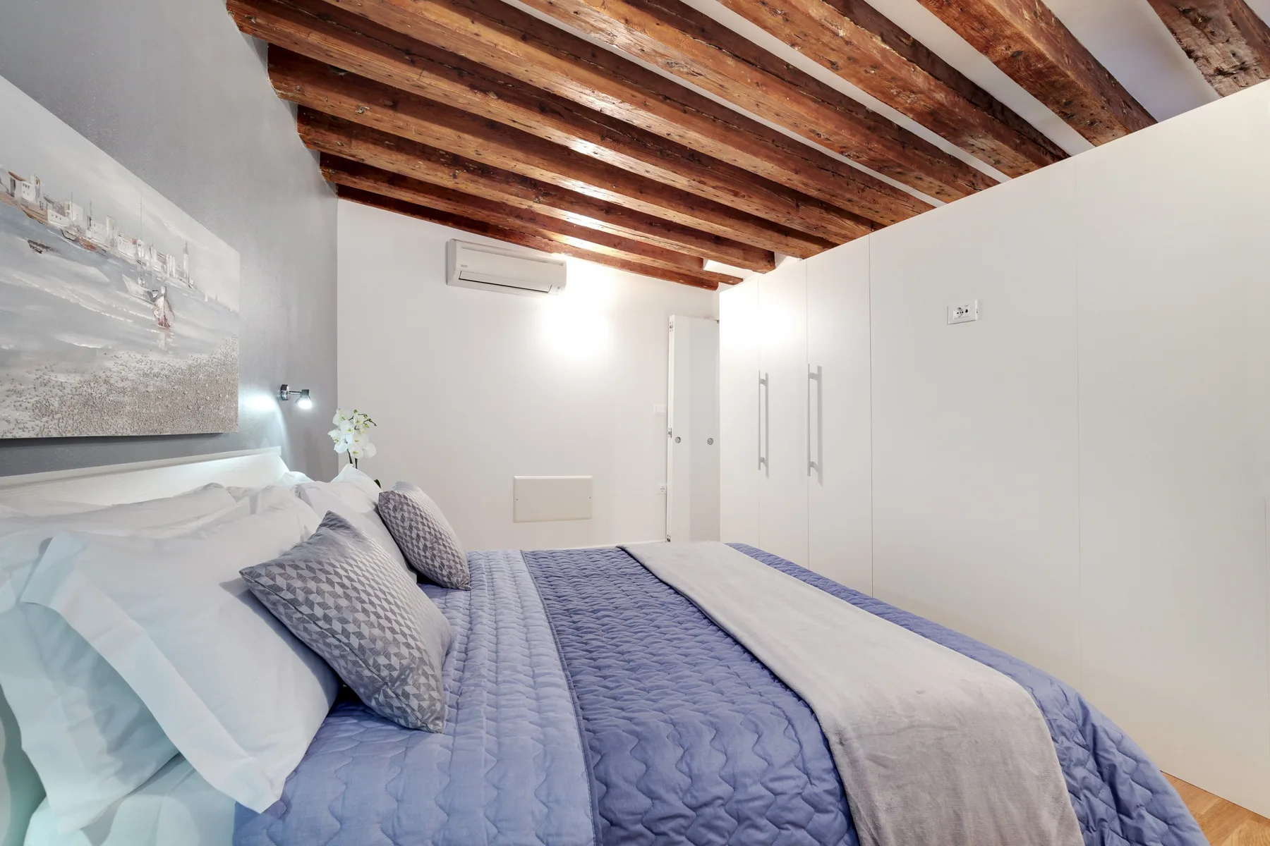 A bedroom with a neatly made bed beneath exposed wooden ceiling beams.