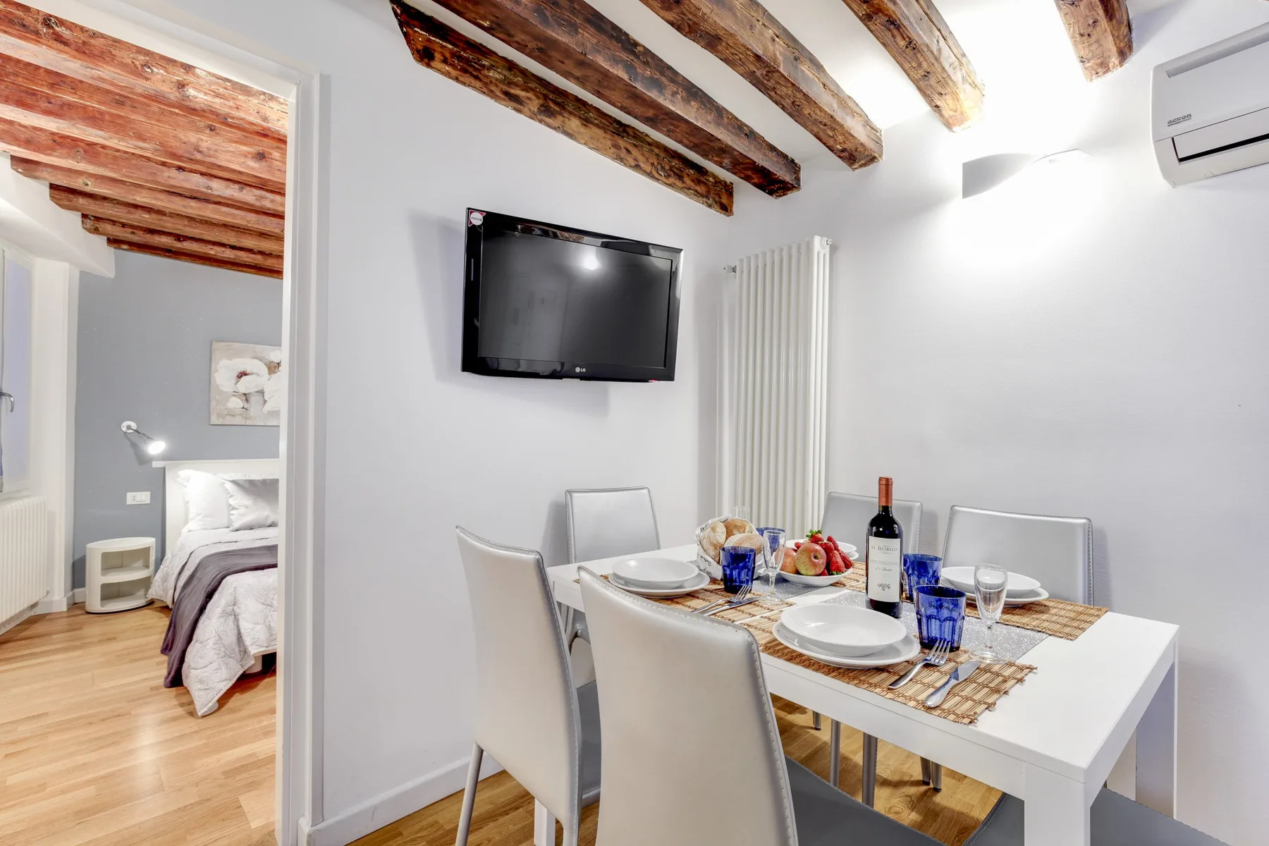A dining area with a white table set with plates and glasses beneath exposed wooden ceiling beams.