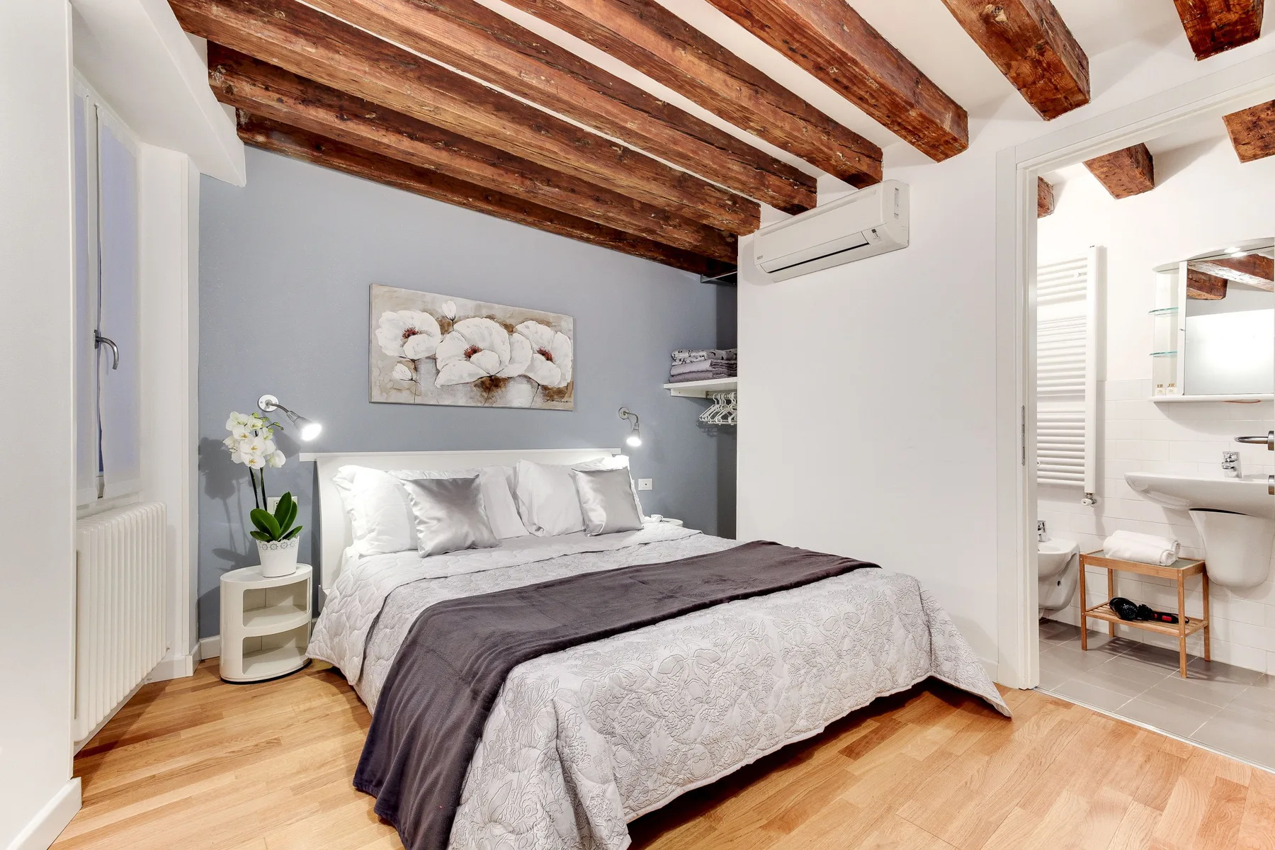 A bedroom with a bed beneath exposed wooden ceiling beams.