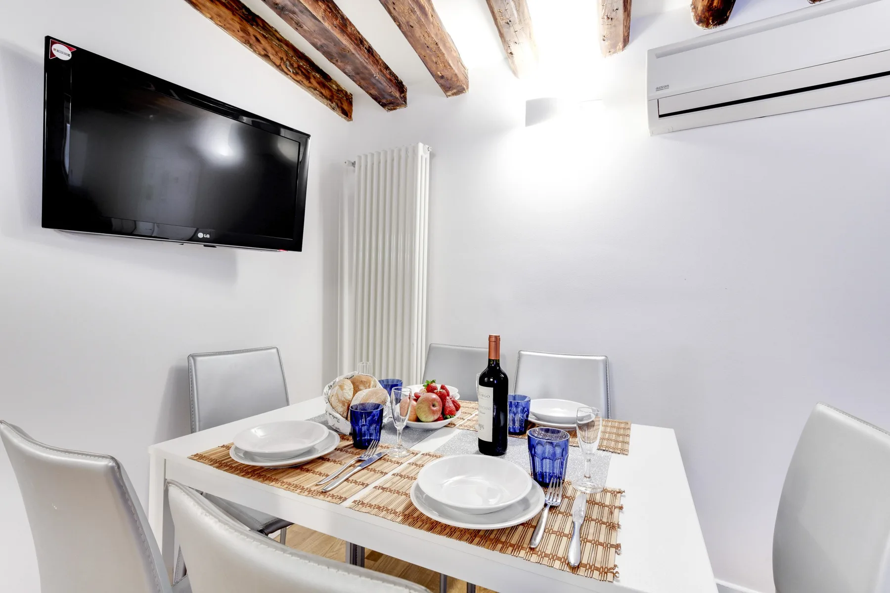 A dining area with a set table, wall-mounted television, and exposed ceiling beams.