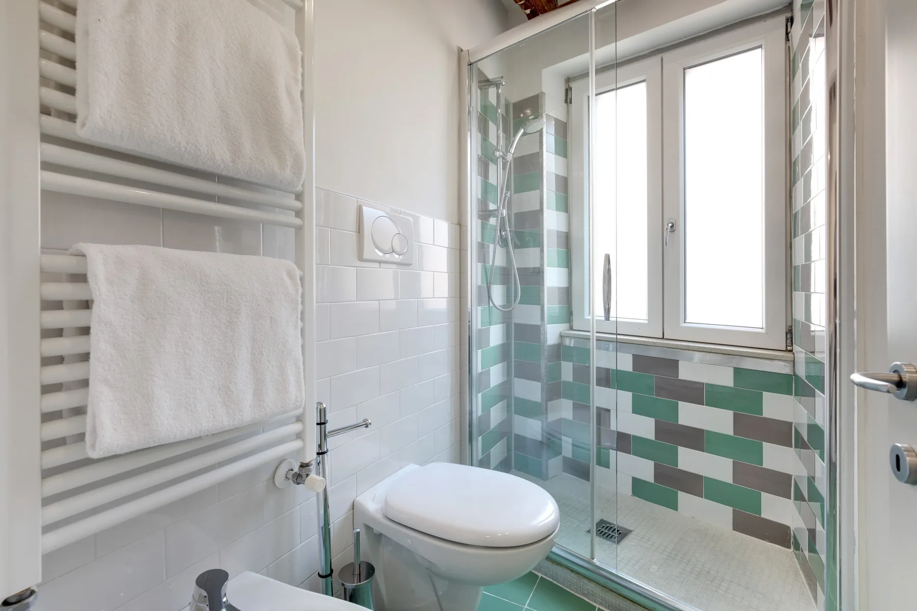A bright bathroom with a glass shower, tiled walls, and a toilet.