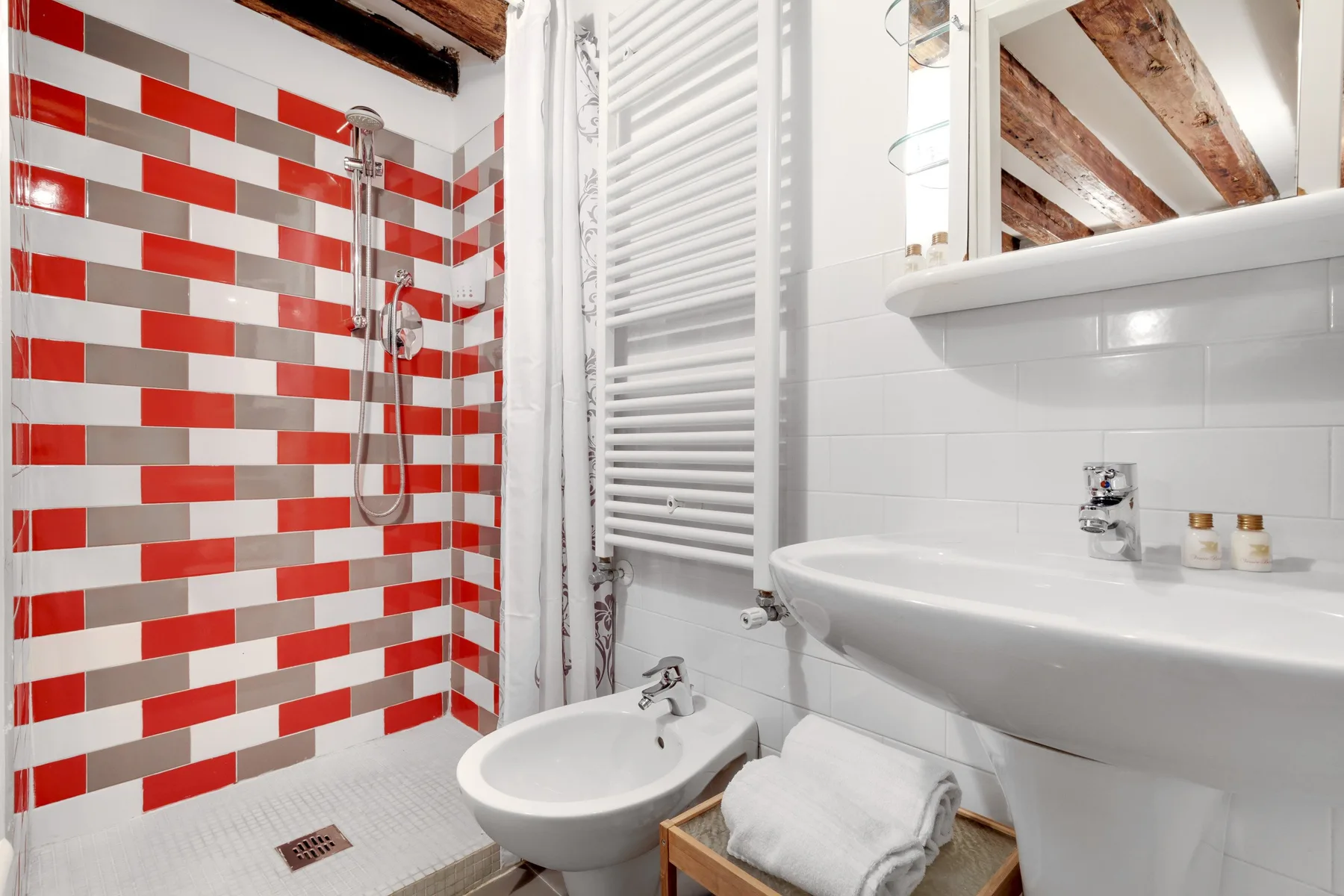 A bathroom with a sink, bidet, and shower lined with red and white tiles.