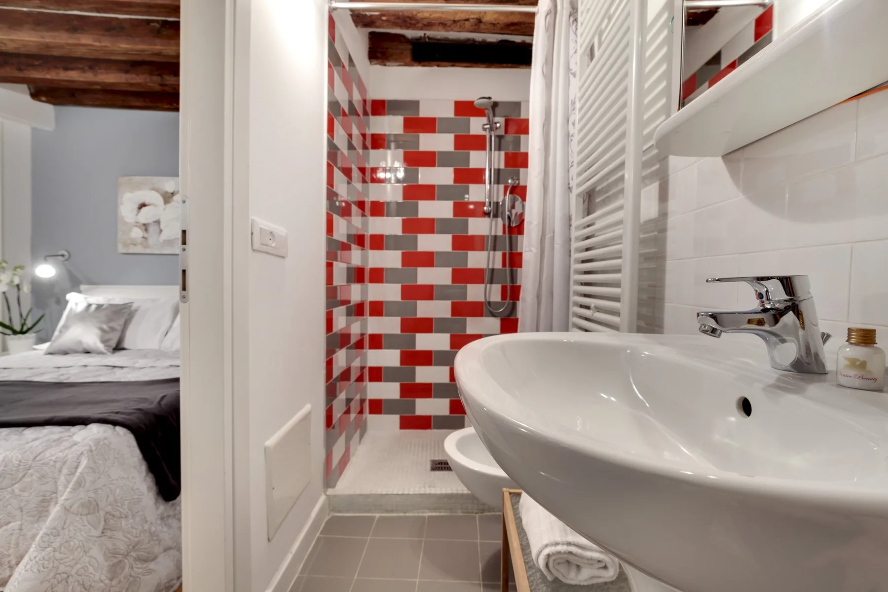 A bathroom with a sink and shower, with a bedroom visible through the doorway.