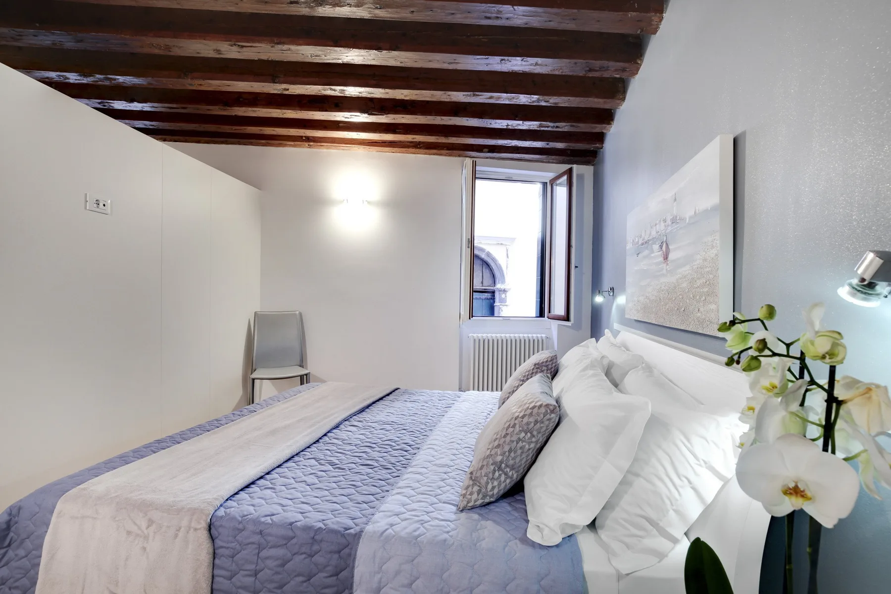 A bedroom with a neatly made bed and exposed ceiling beams.