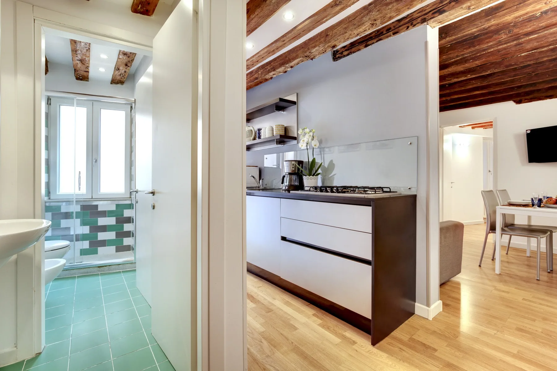 A compact kitchen opens onto a dining area, with a tiled bathroom visible nearby.