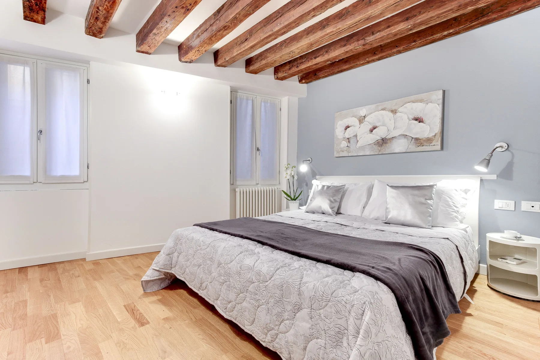 A bright bedroom with a bed beneath exposed wooden ceiling beams.