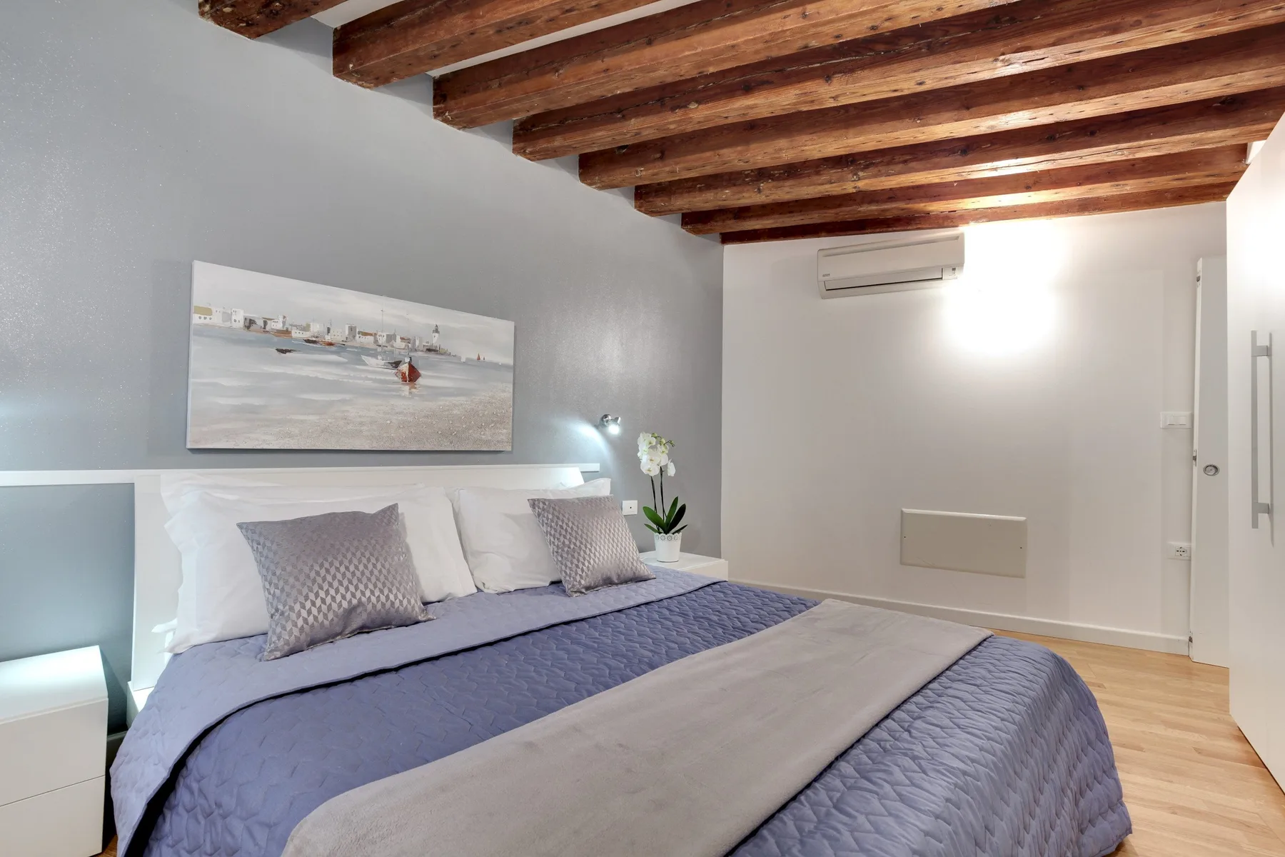 A bedroom with a neatly made bed and exposed wooden ceiling beams.