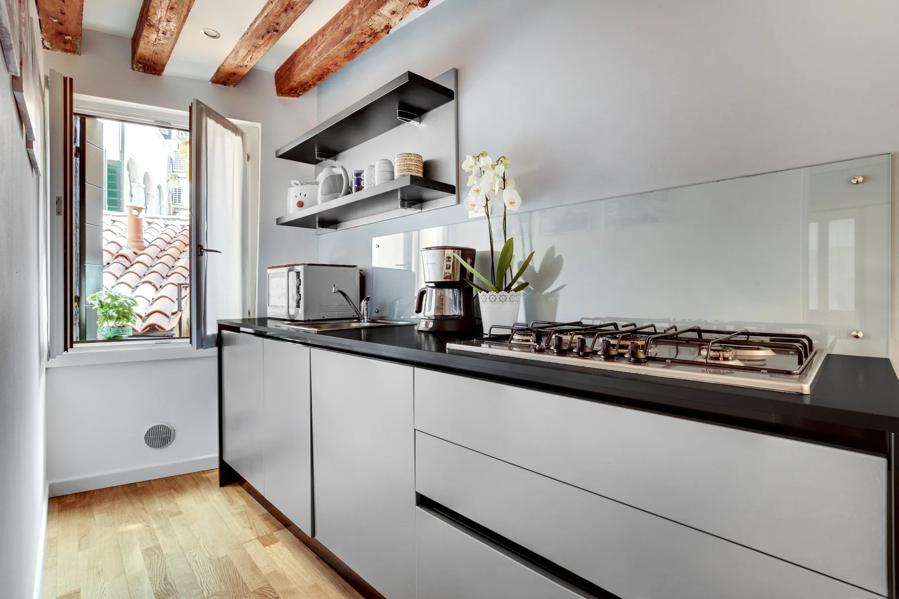 A modern kitchen with a long counter, cooktop, and open shelves.