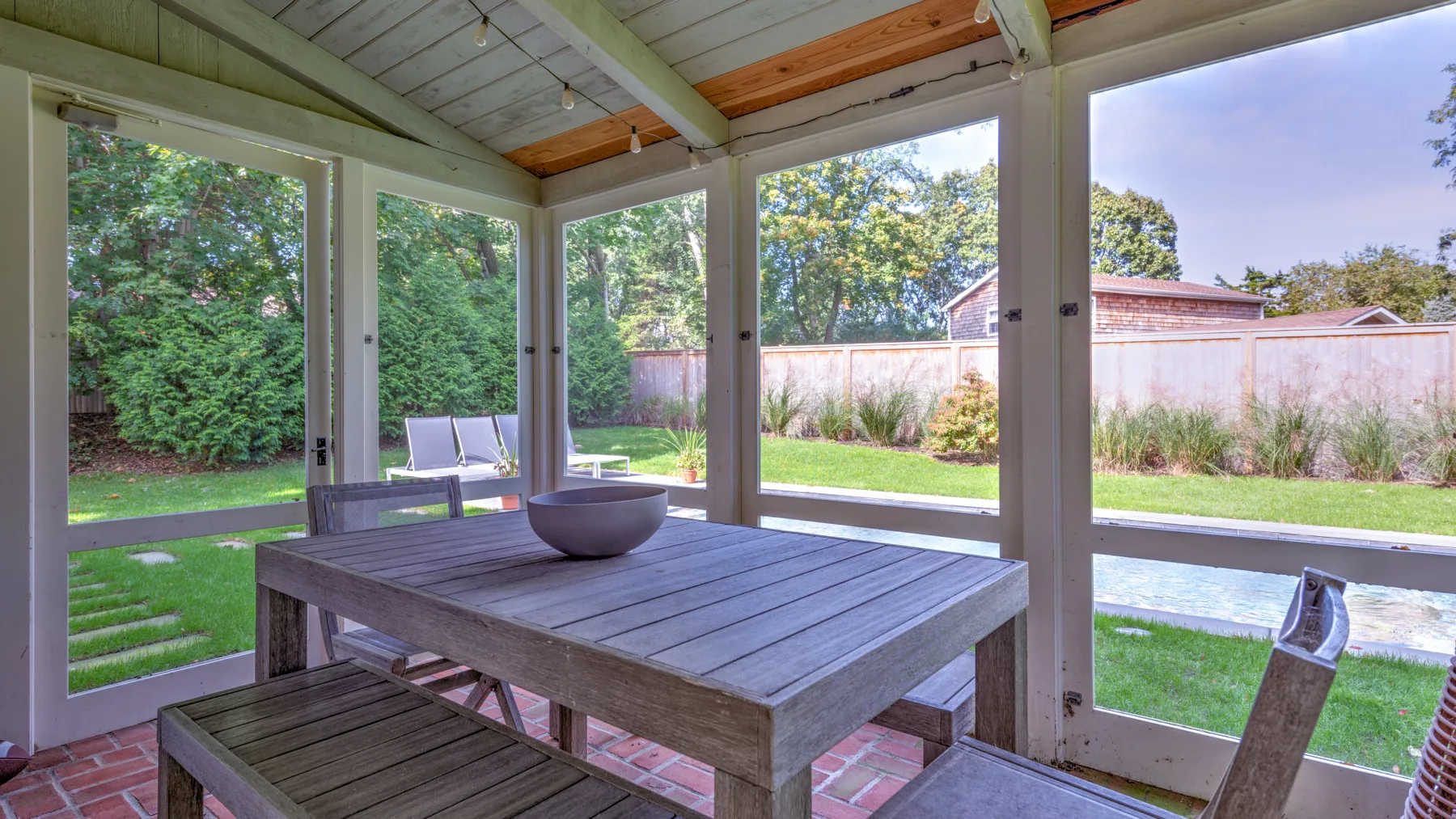 Un patio cubierto con una mesa de madera y asientos da a un jardín.