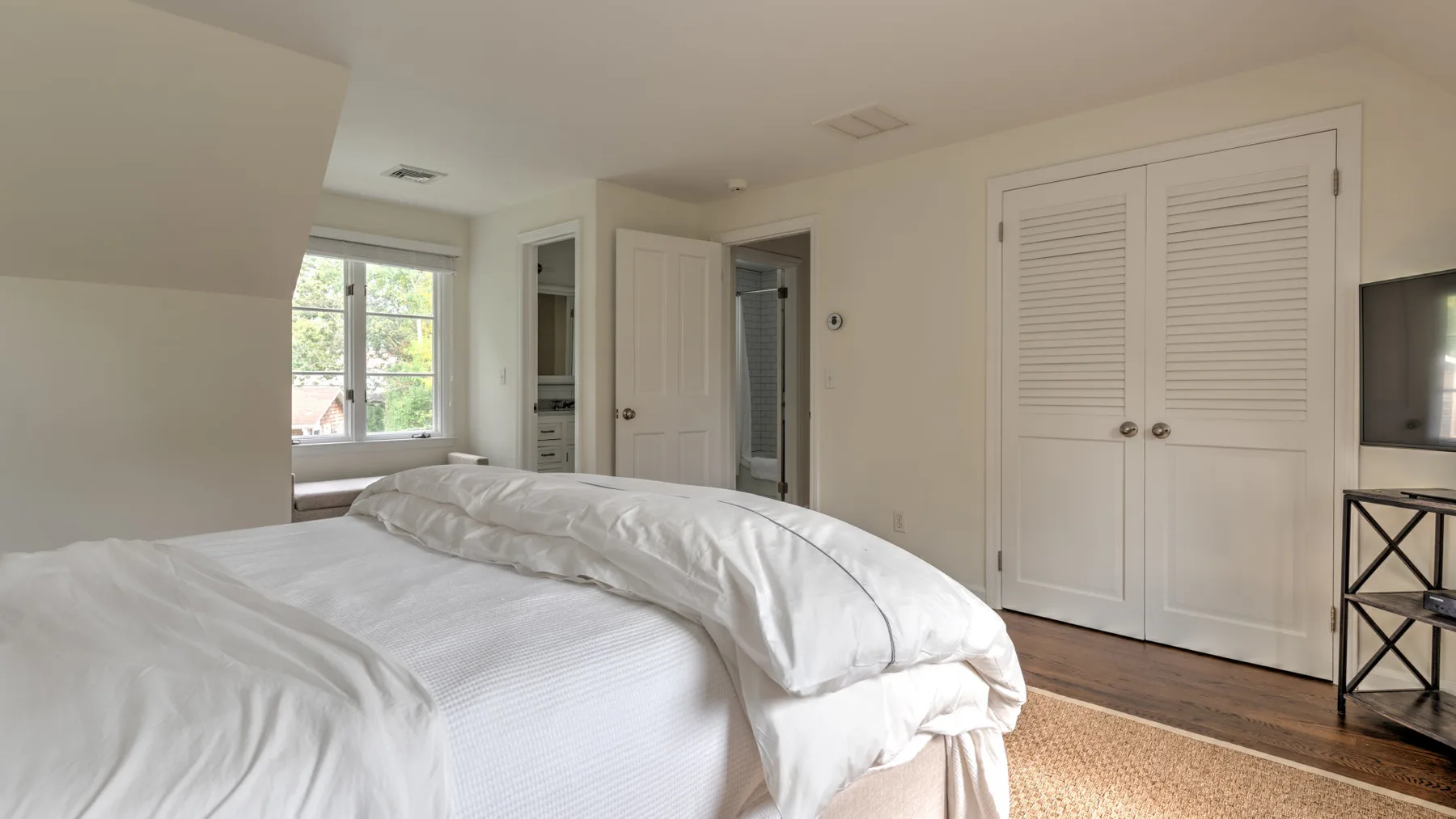 Un dormitorio con una cama bien tendida junto a una ventana.