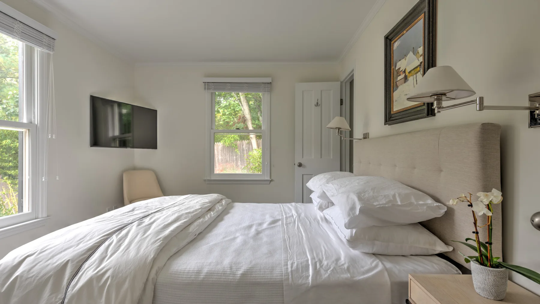 Un dormitorio luminoso con una cama bien tendida y ventanas con vistas a la vegetación.