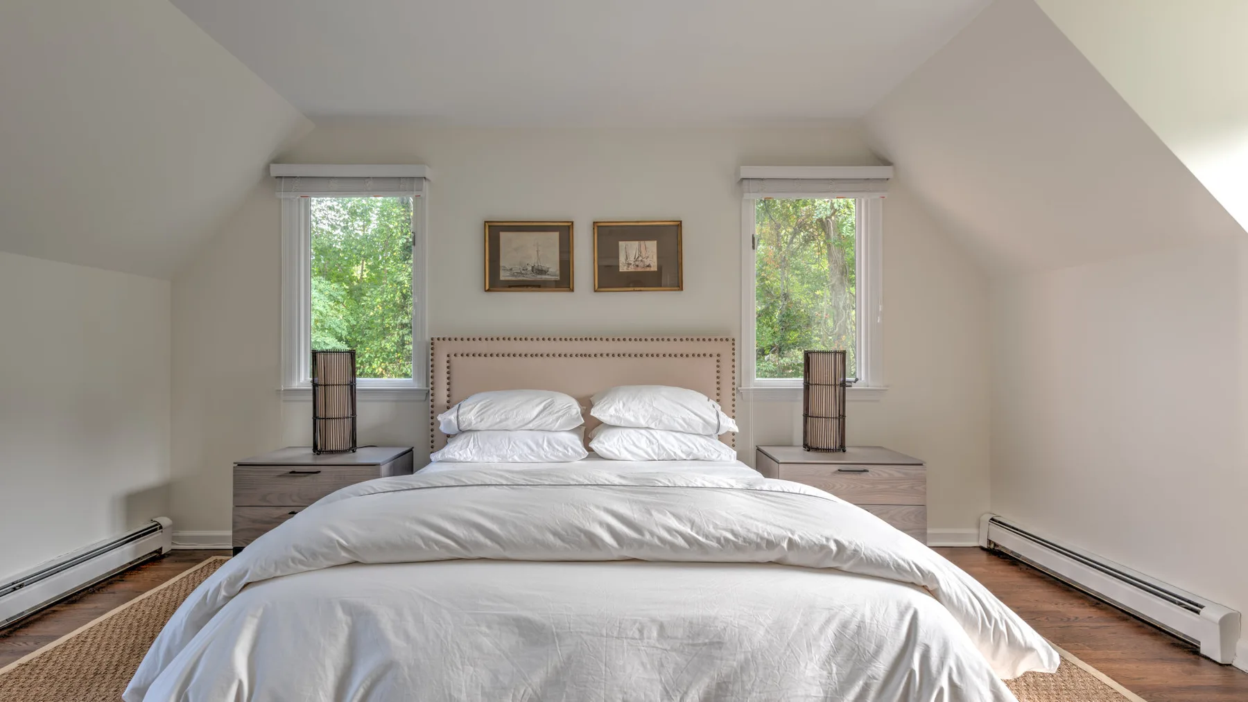 Un dormitorio luminoso con una cama tendida entre dos ventanas.