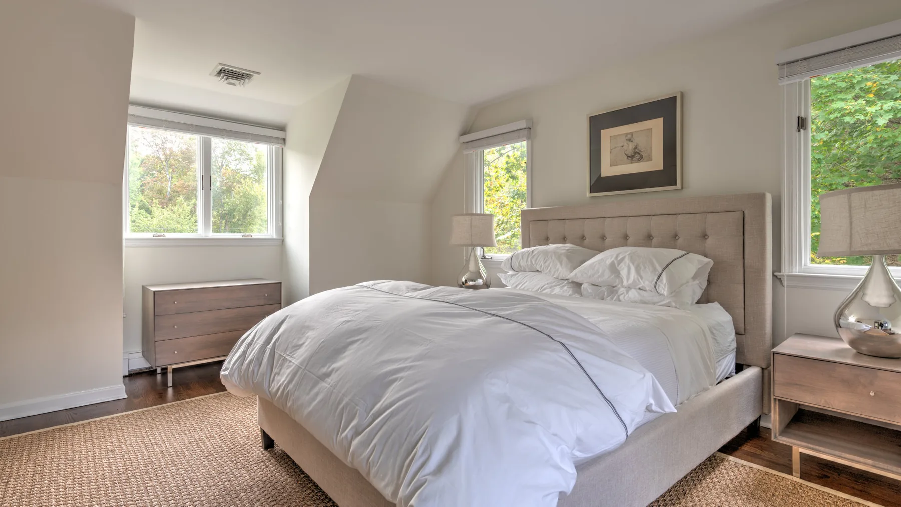 Un dormitorio luminoso con una cama grande, mesillas de noche y ventanas con vistas a la vegetación.