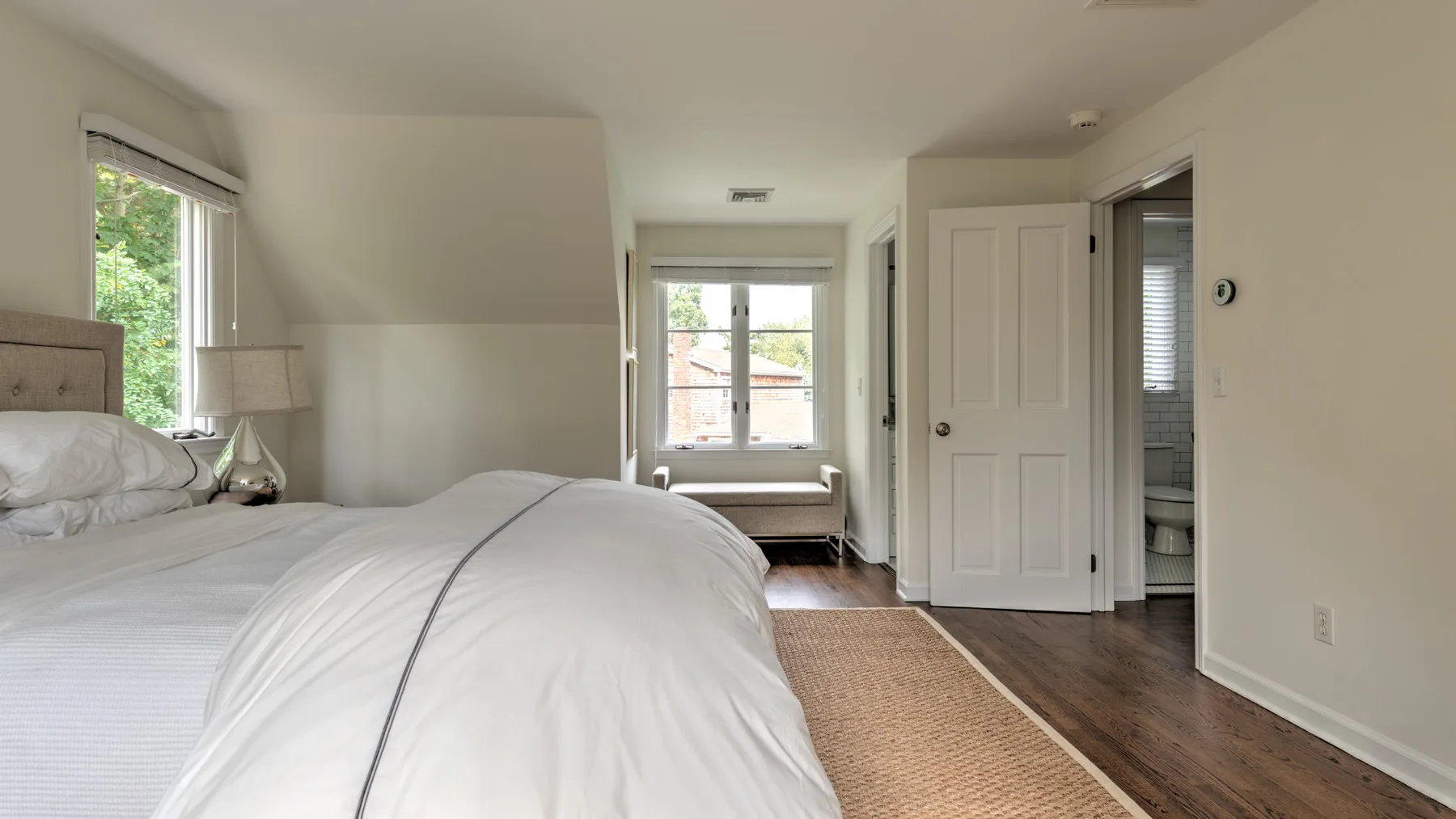 Un dormitorio luminoso con una cama, ventanas y una puerta abierta.