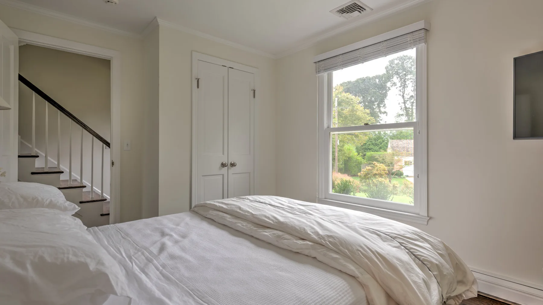 Un dormitorio con una cama junto a una ventana amplia con vistas a la vegetación.