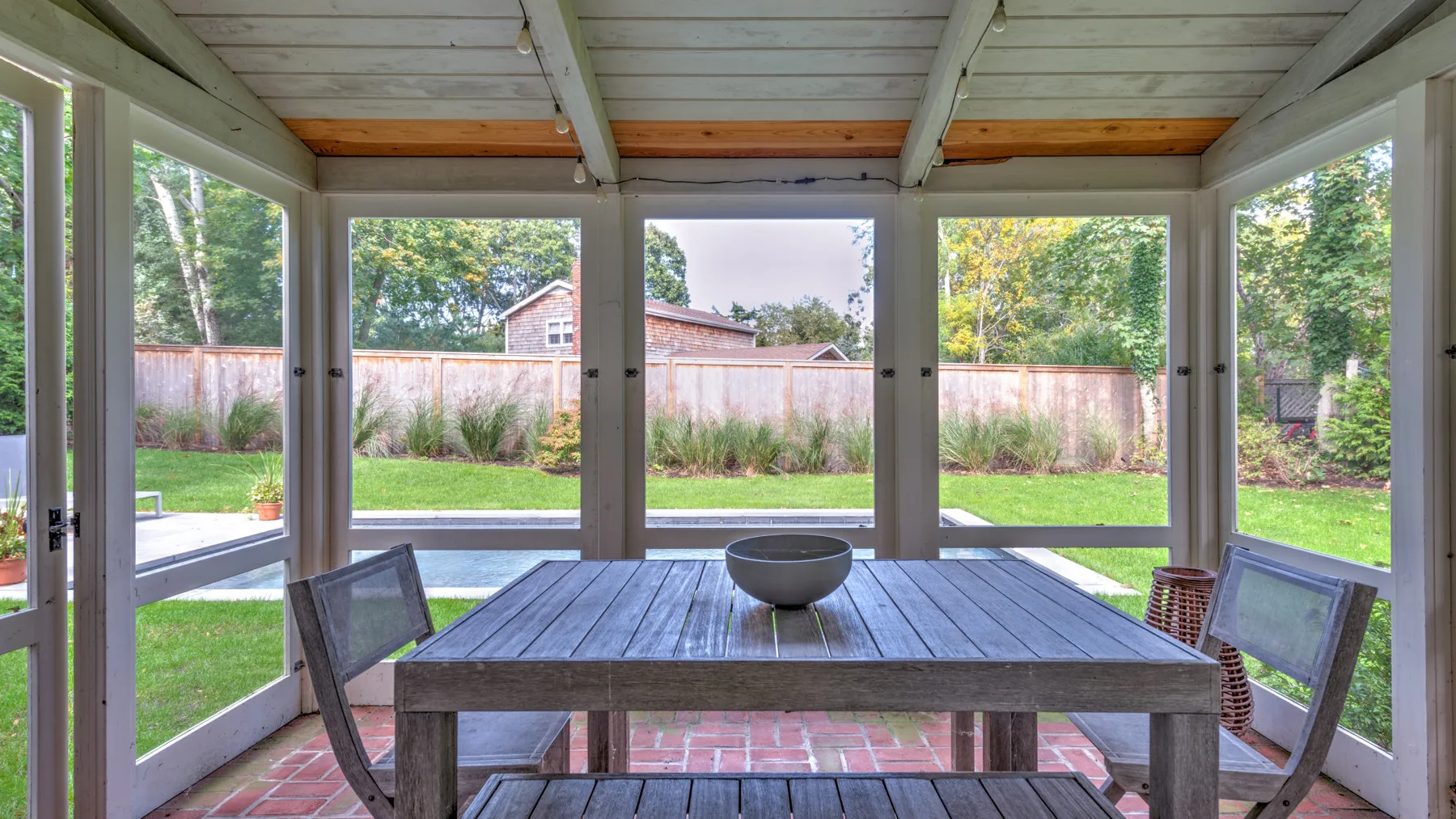 Un patio cubierto con una mesa de comedor de madera rodeada de grandes ventanas.