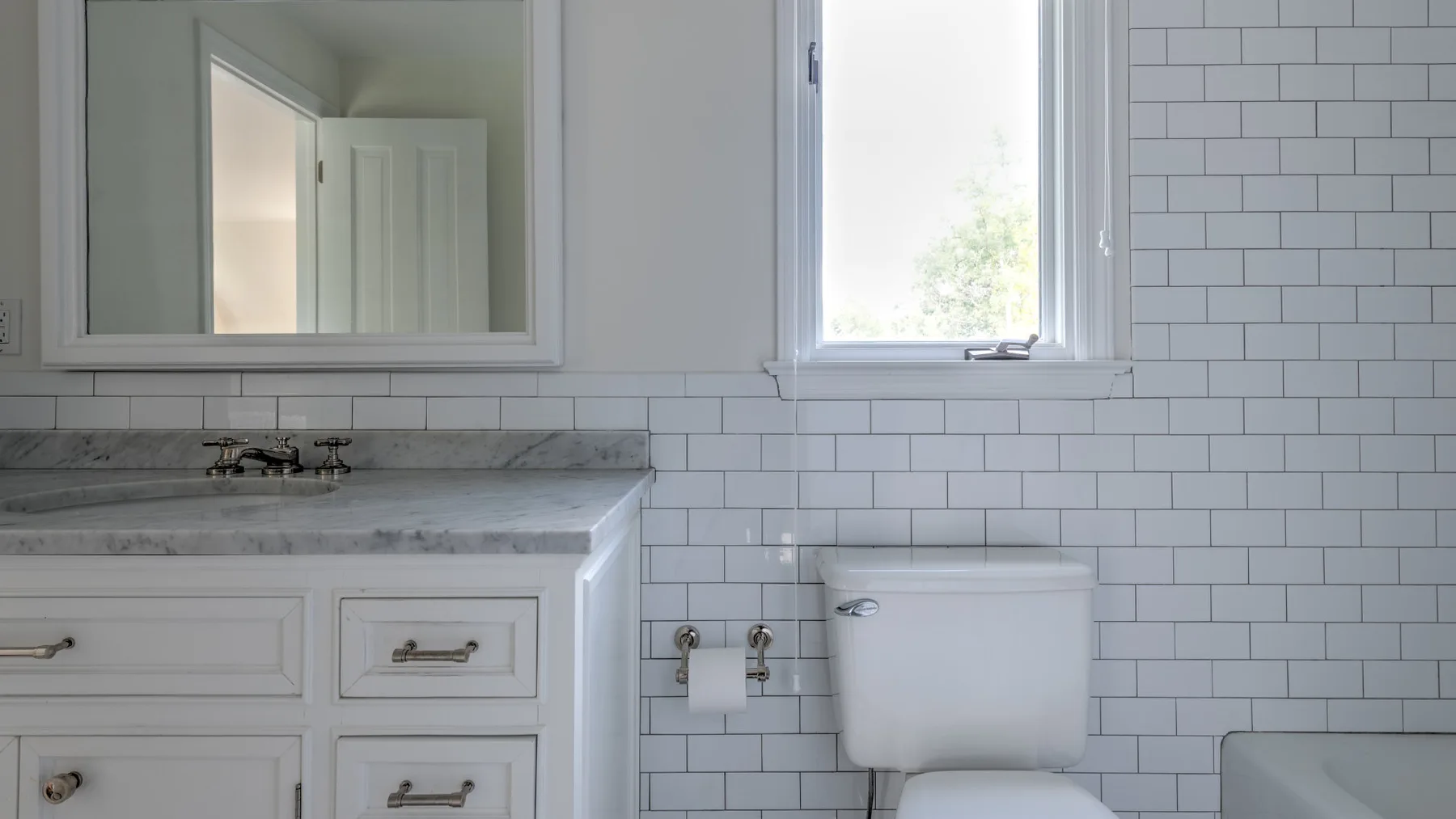 Un baño alicatado con lavabo, espejo e inodoro junto a una ventana.