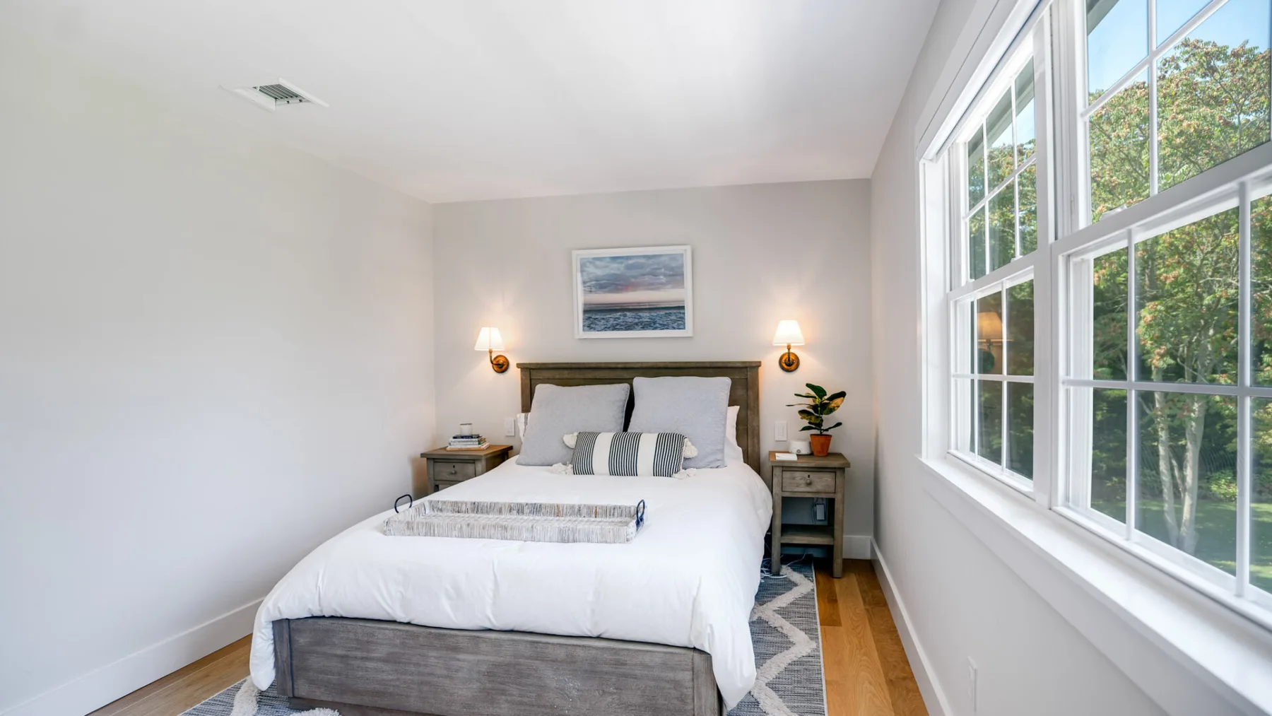 Un dormitorio luminoso con una cama bien tendida junto a grandes ventanas.