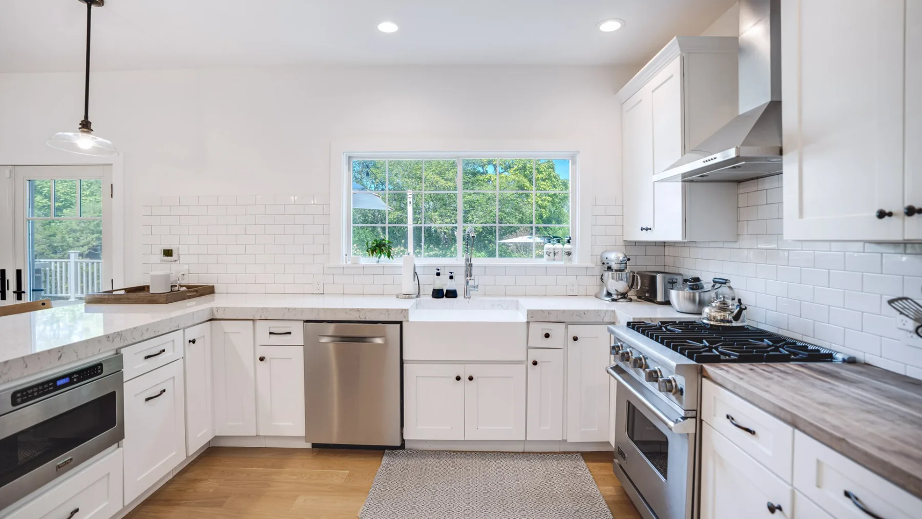 Una cocina luminosa con gabinetes blancos, electrodomésticos de acero inoxidable y una ventana grande.