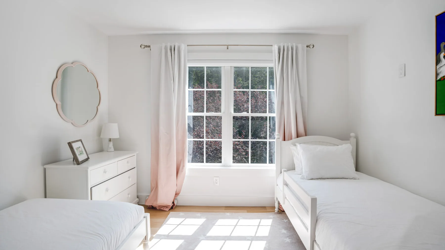 Un dormitorio luminoso con dos camas, una cómoda y una ventana grande.