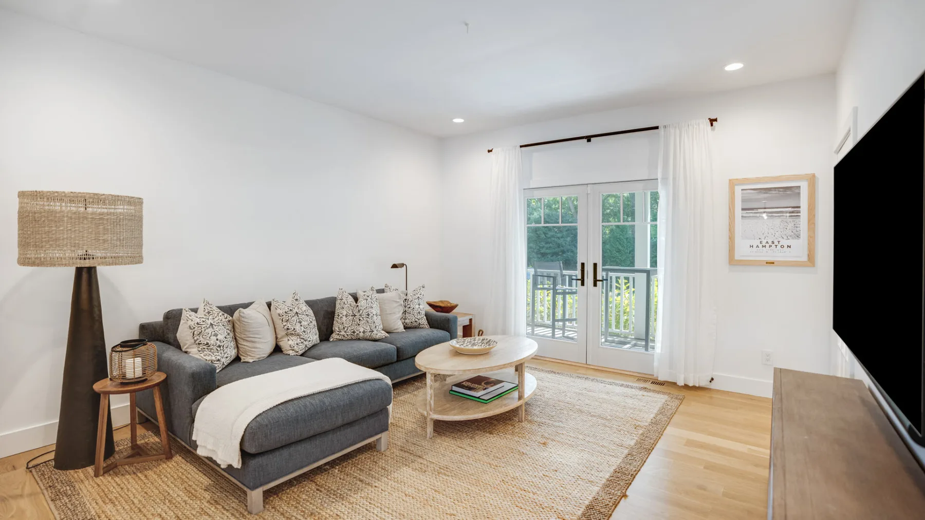 Una sala luminosa con sofá seccional, mesa de centro y puertas de vidrio que dan a un balcón.