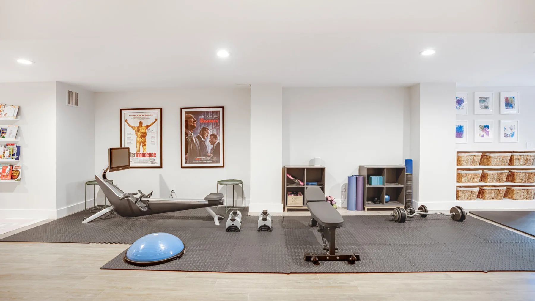 Un gimnasio luminoso con equipo de ejercicio y cuadros en las paredes.