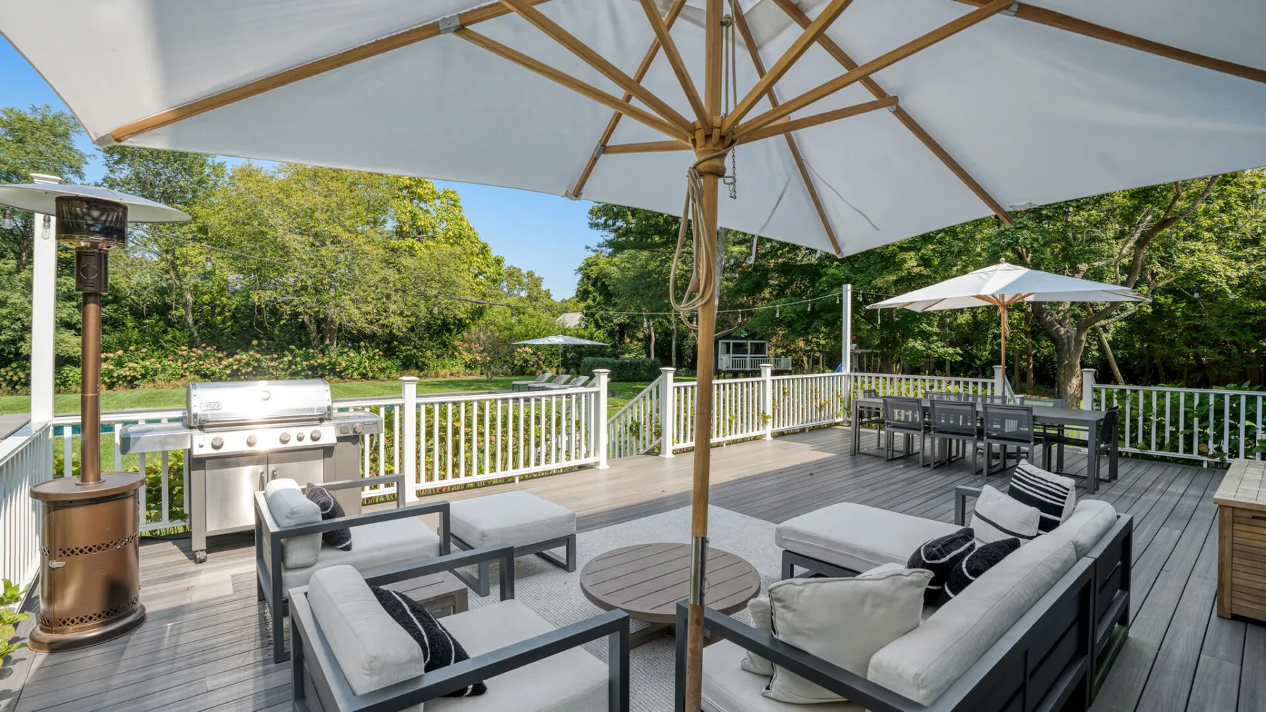 Una terraza exterior tiene asientos, una mesa de comedor y sombrillas grandes.
