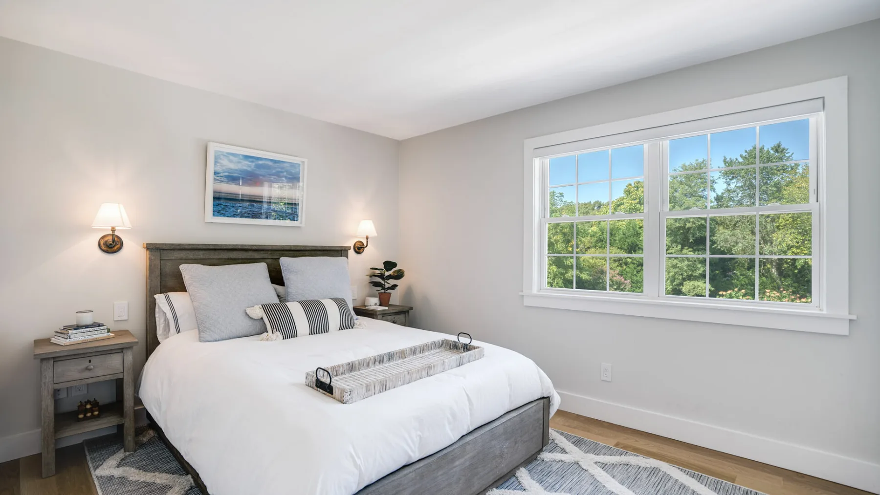 Un dormitorio luminoso con una cama tendida junto a una ventana grande.