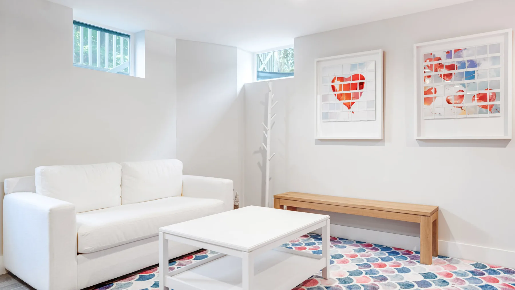Una sala luminosa con asientos blancos, una mesa de centro y cuadros coloridos.
