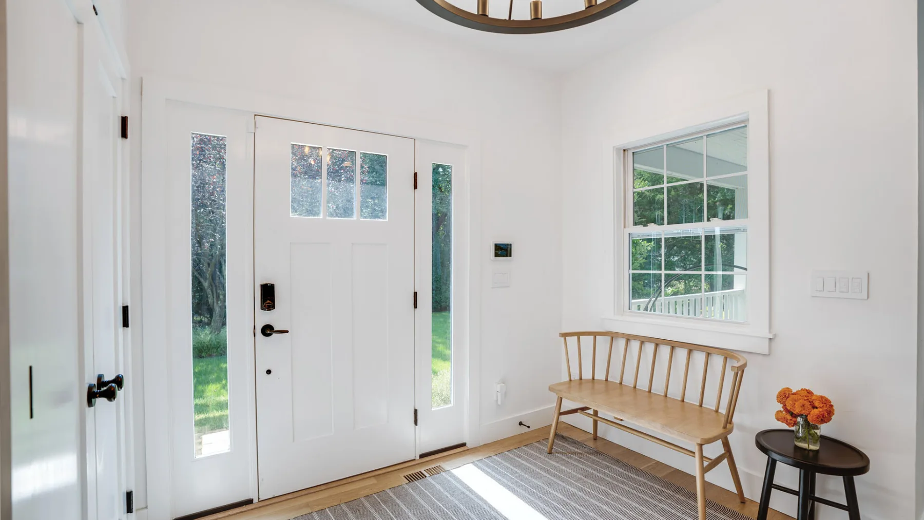 Una entrada luminosa con una puerta principal, un banco de madera y una ventana.