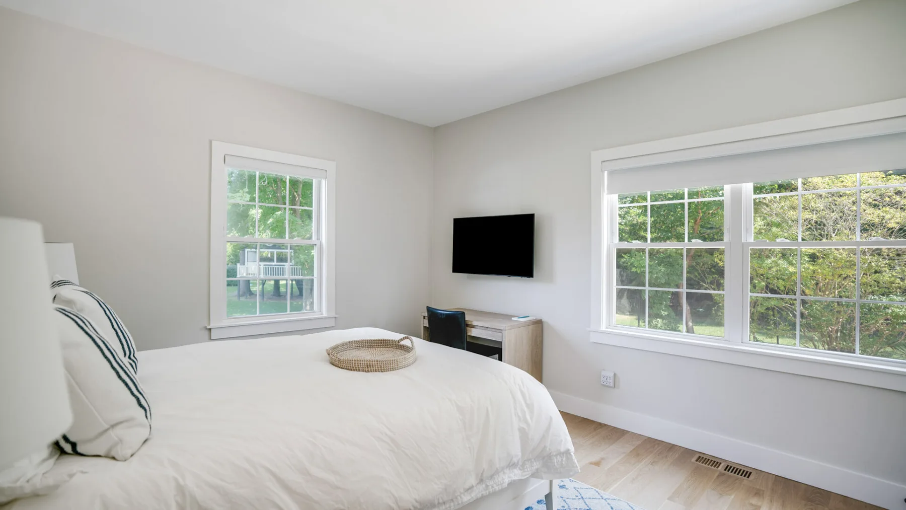 Un dormitorio luminoso con una cama, un televisor y ventanas con vista a la vegetación.