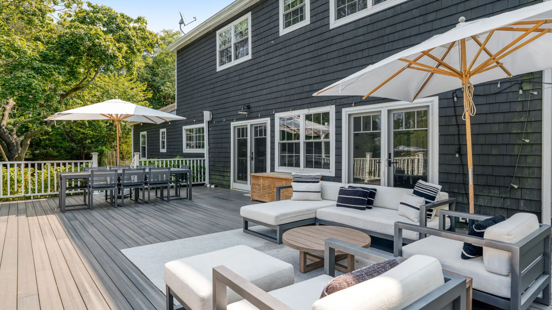 Una amplia terraza exterior con asientos, muebles de comedor y grandes sombrillas.