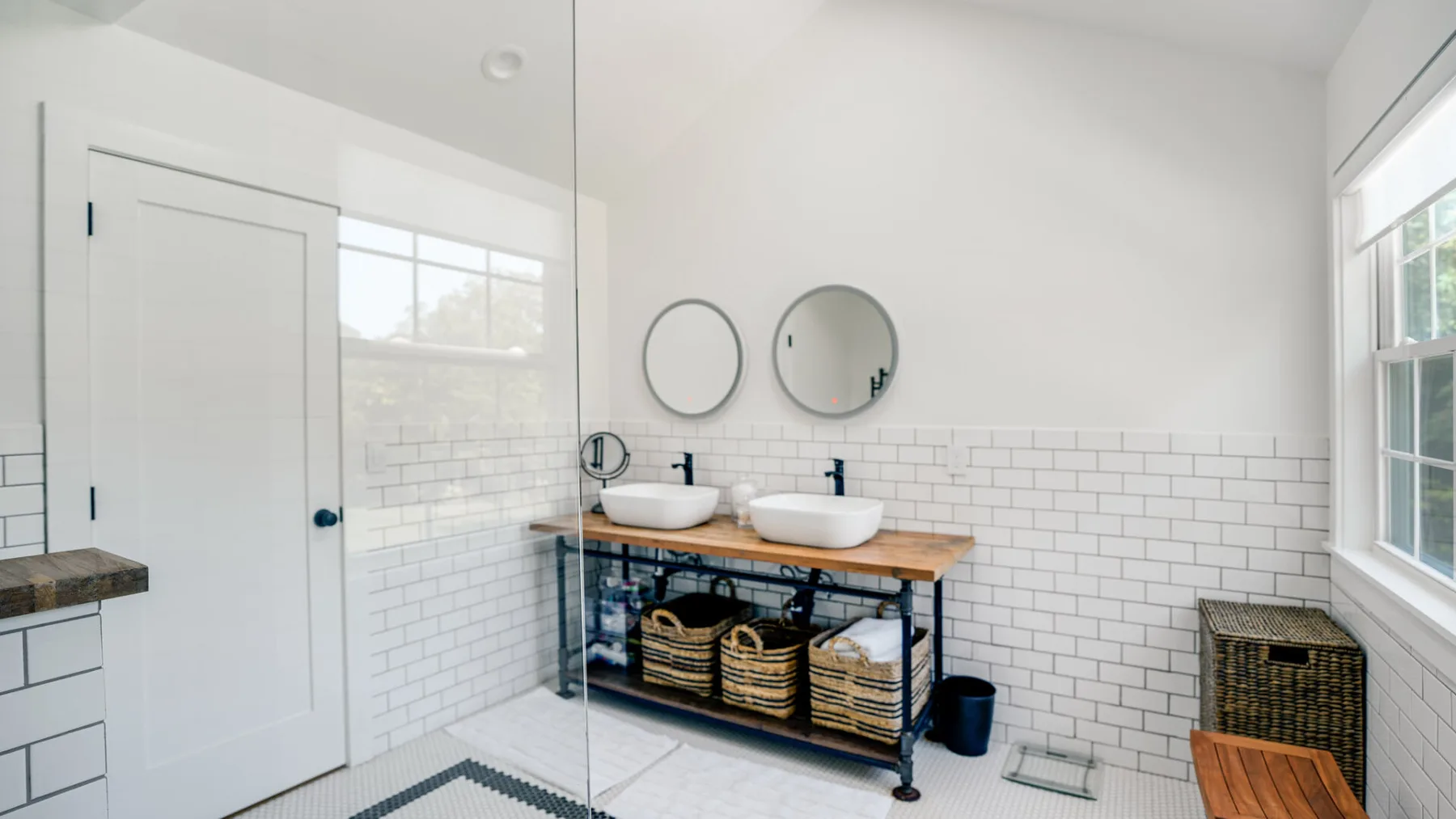 Un baño luminoso con dos lavabos, paredes de azulejos y un panel de ducha de vidrio.