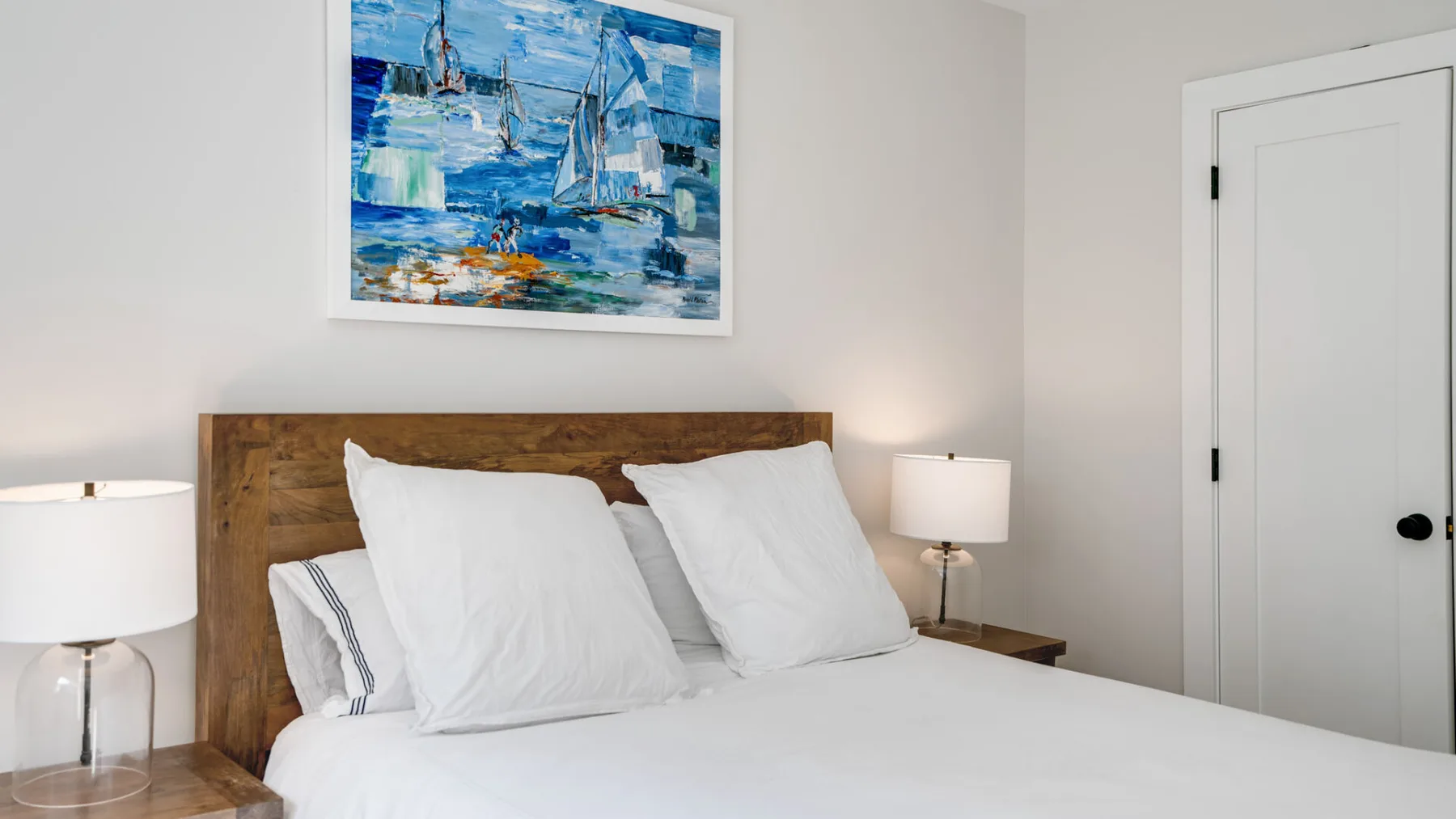 Un dormitorio con una cama, ropa de cama blanca y un cuadro colorido sobre el cabecero.