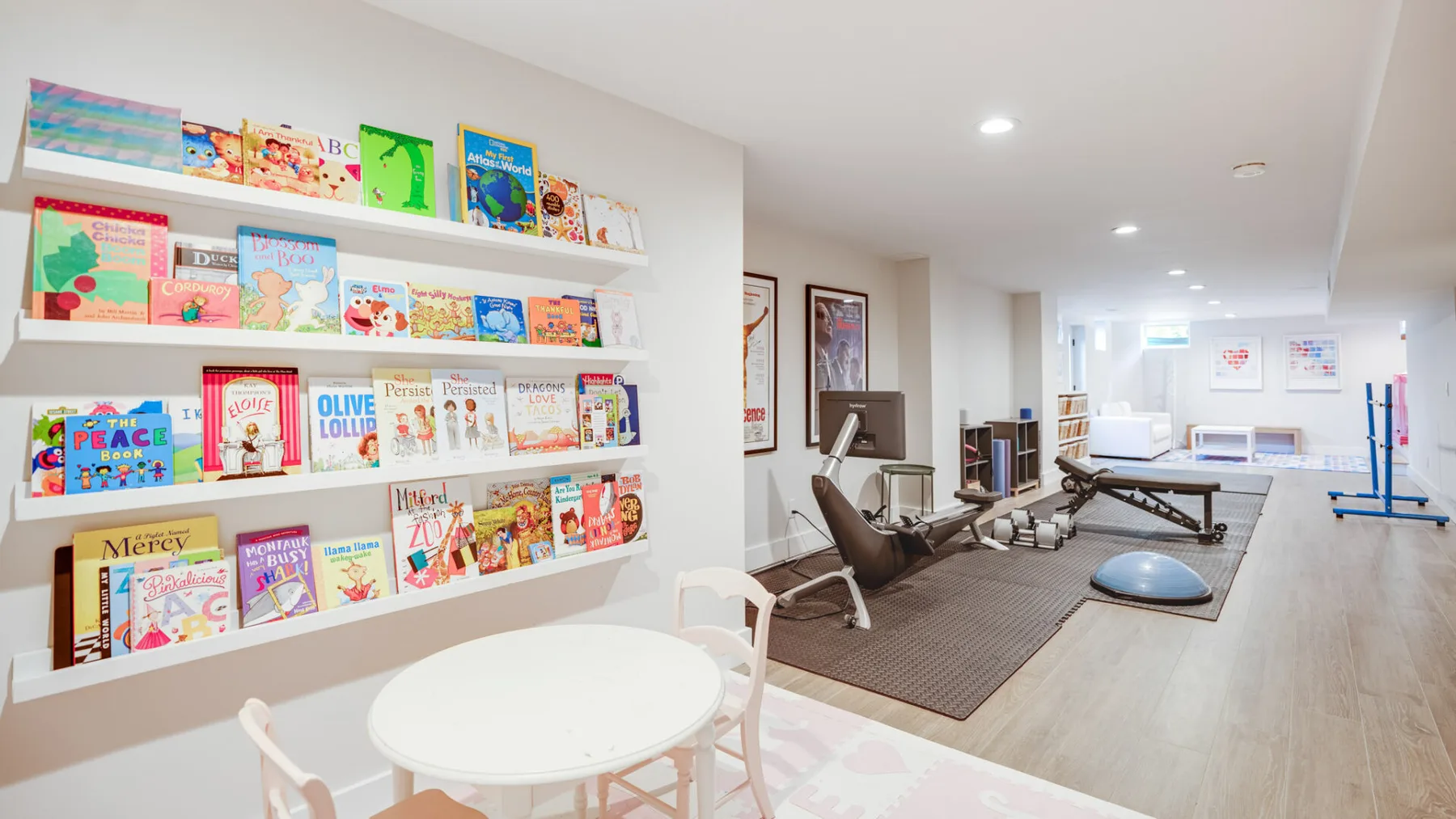 Una sala de juegos luminosa con libros en estantes de pared y una mesa pequeña con sillas.