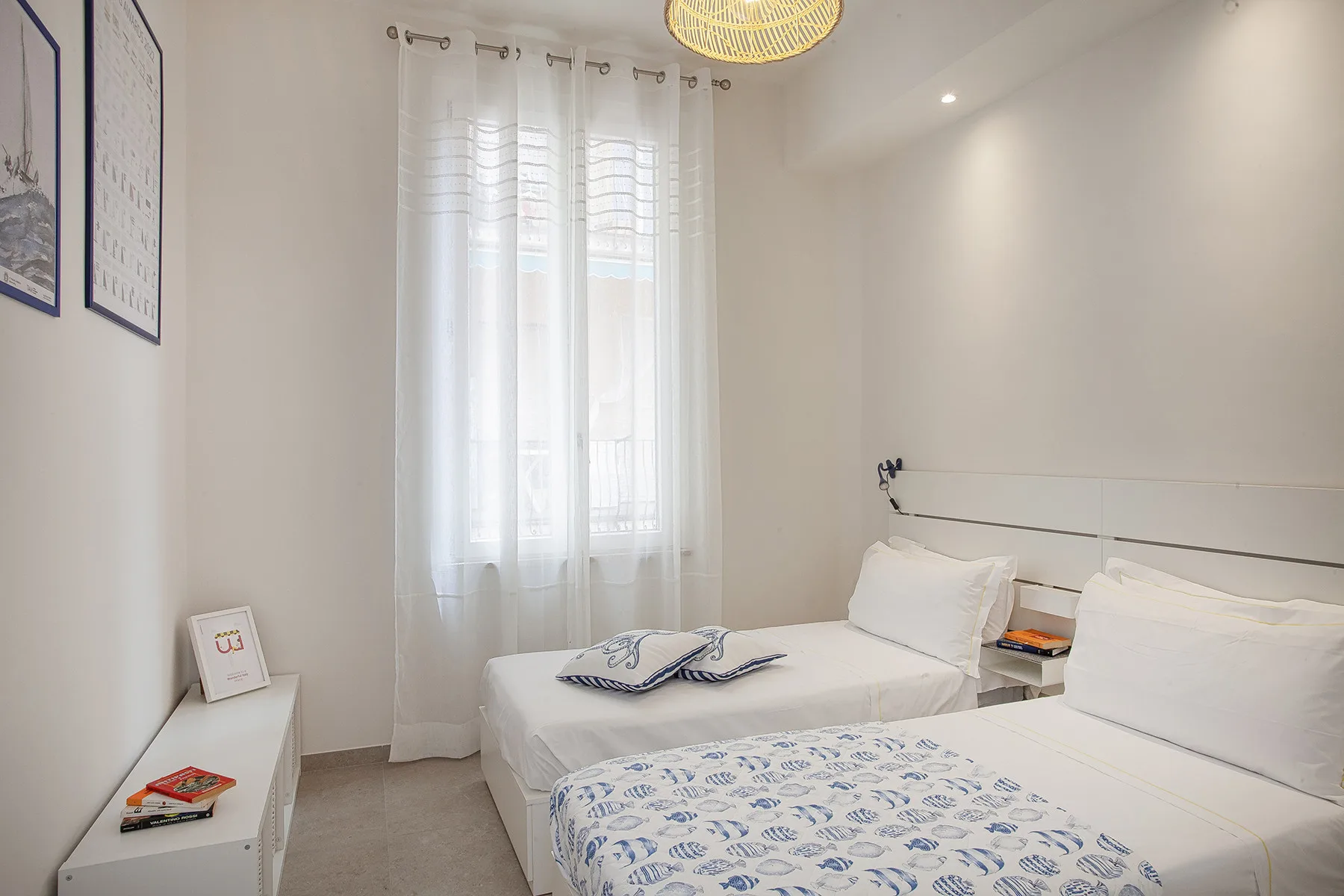 Un dormitorio luminoso con dos camas y cortinas translúcidas en la ventana.