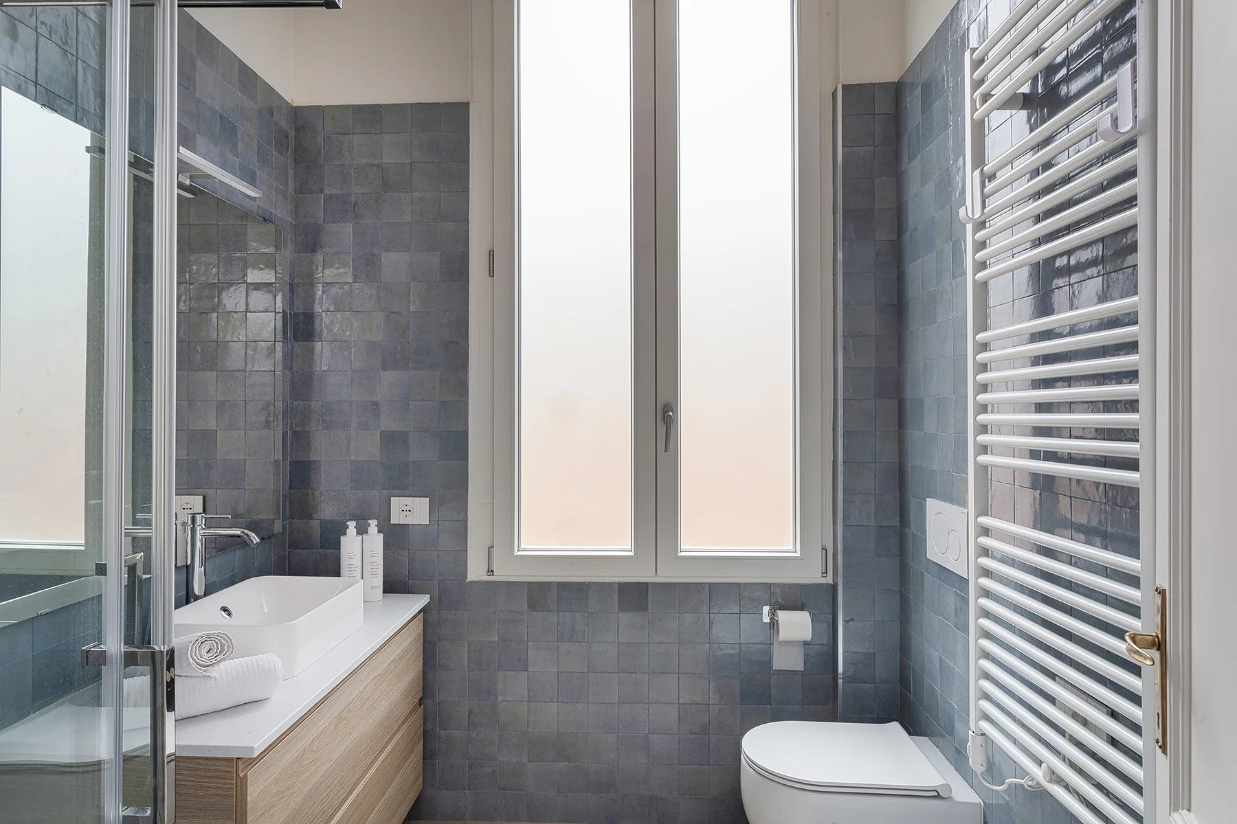 Un baño alicatado con bañera, inodoro y ventanas altas.