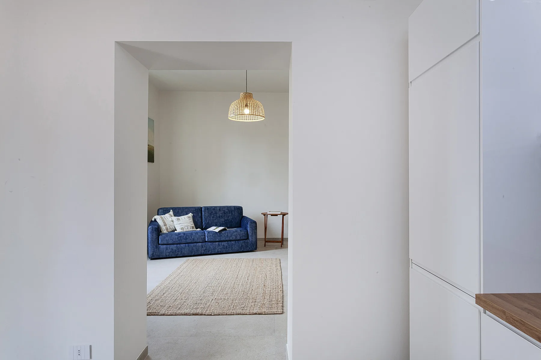 Un pasillo blanco se abre a una sala de estar con asientos azules y una alfombra tejida.