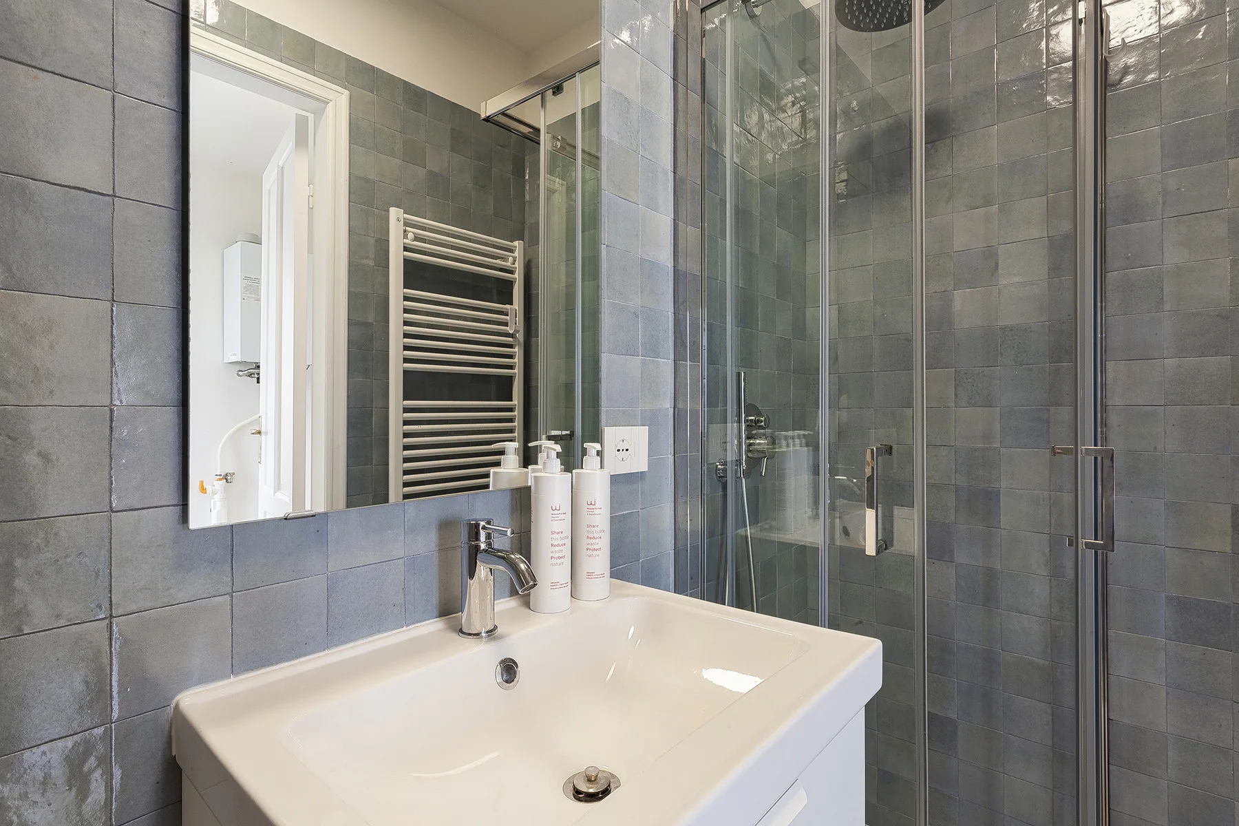 Un baño con azulejos, un lavabo blanco y una ducha de vidrio.