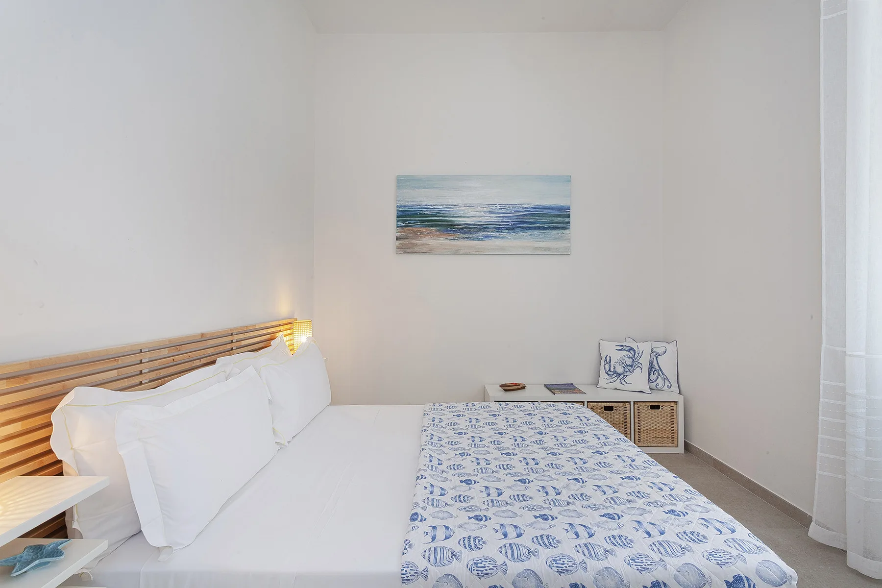 Un dormitorio luminoso con una cama vestida con ropa de cama blanca y estampada en azul.