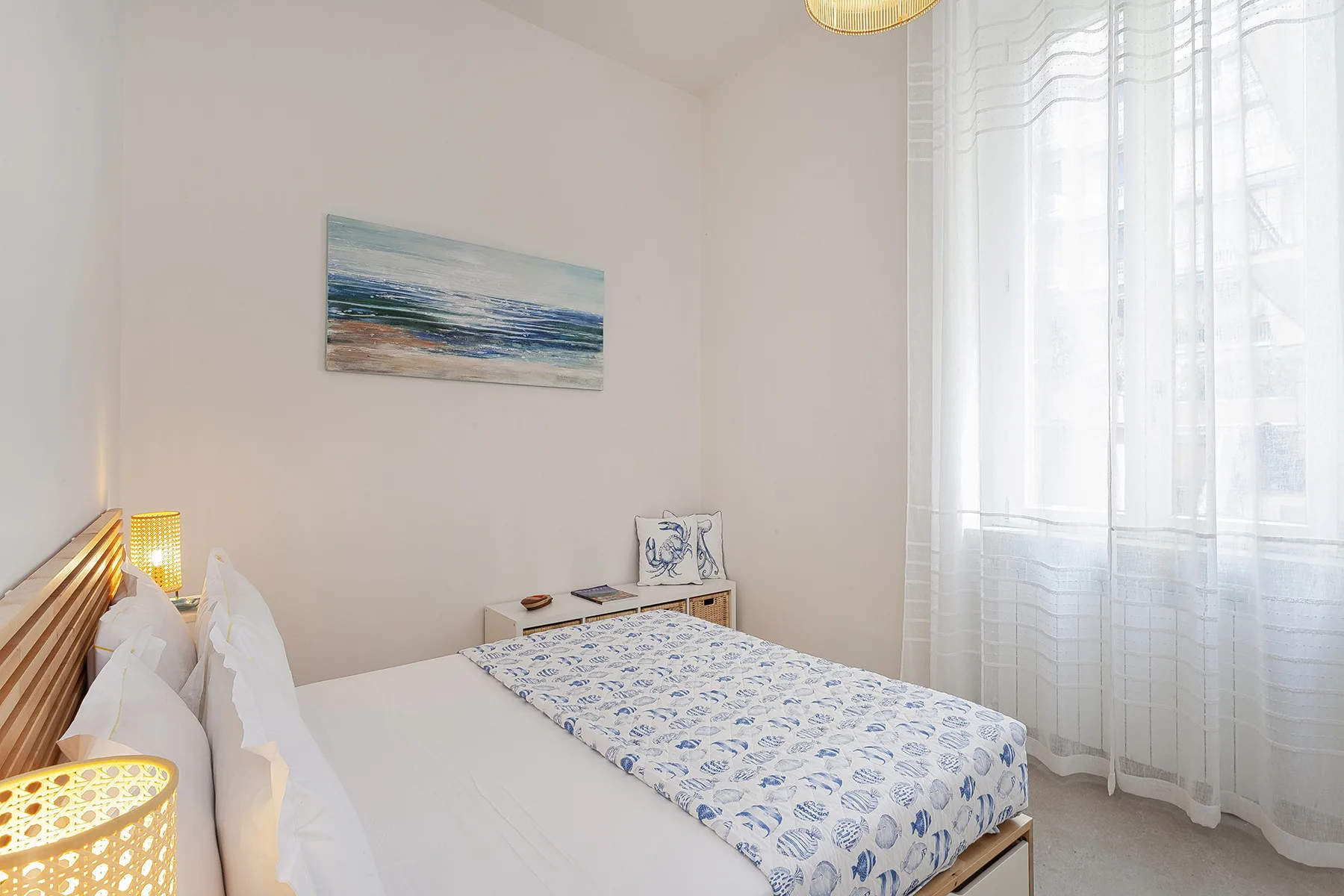 Un dormitorio con una cama cubierta con ropa de cama estampada en azul y blanco junto a una ventana alta.